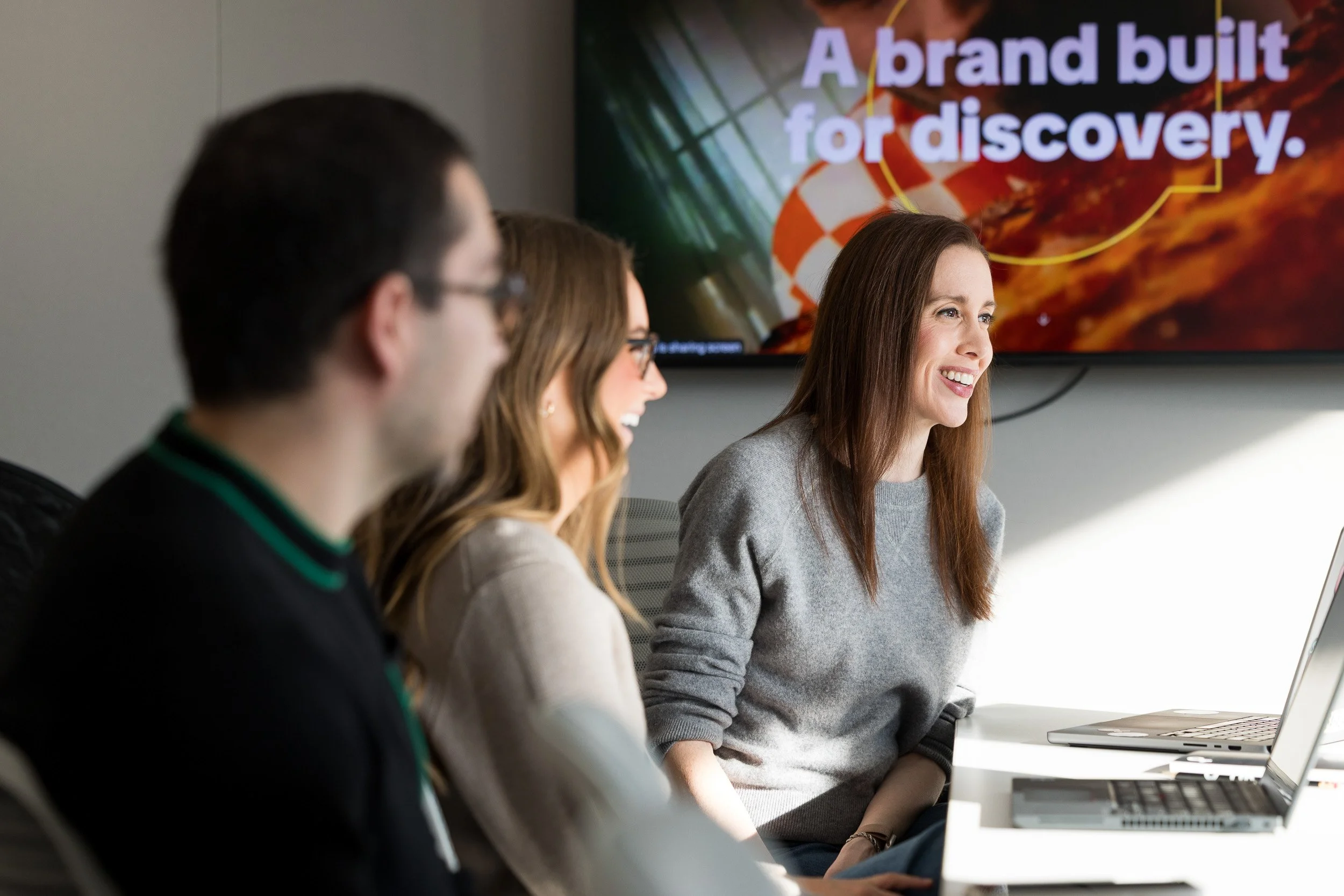 Corporate lifestyle photography of three people sitting at a conference room table in a meeting with a laptop on the table. 