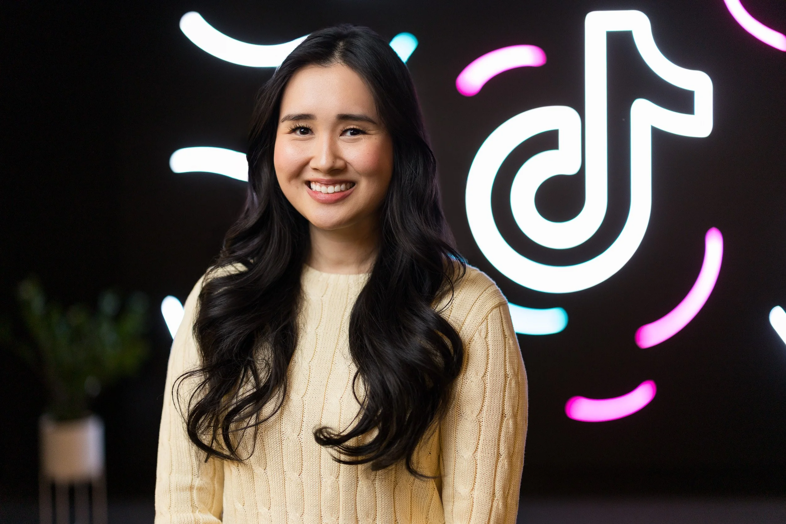 Creative corporate headshot of young Asian female employee with TikTok logo in neon lights in the background