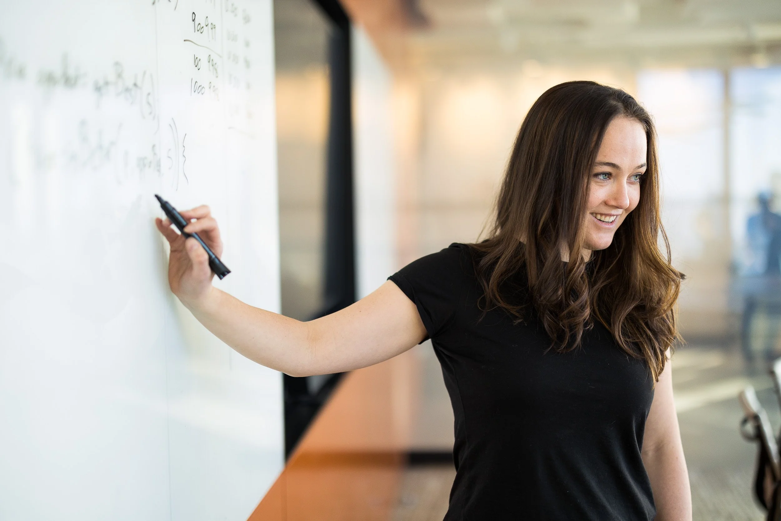 Young female employee gesturing to a whiteboard as she presents information. 