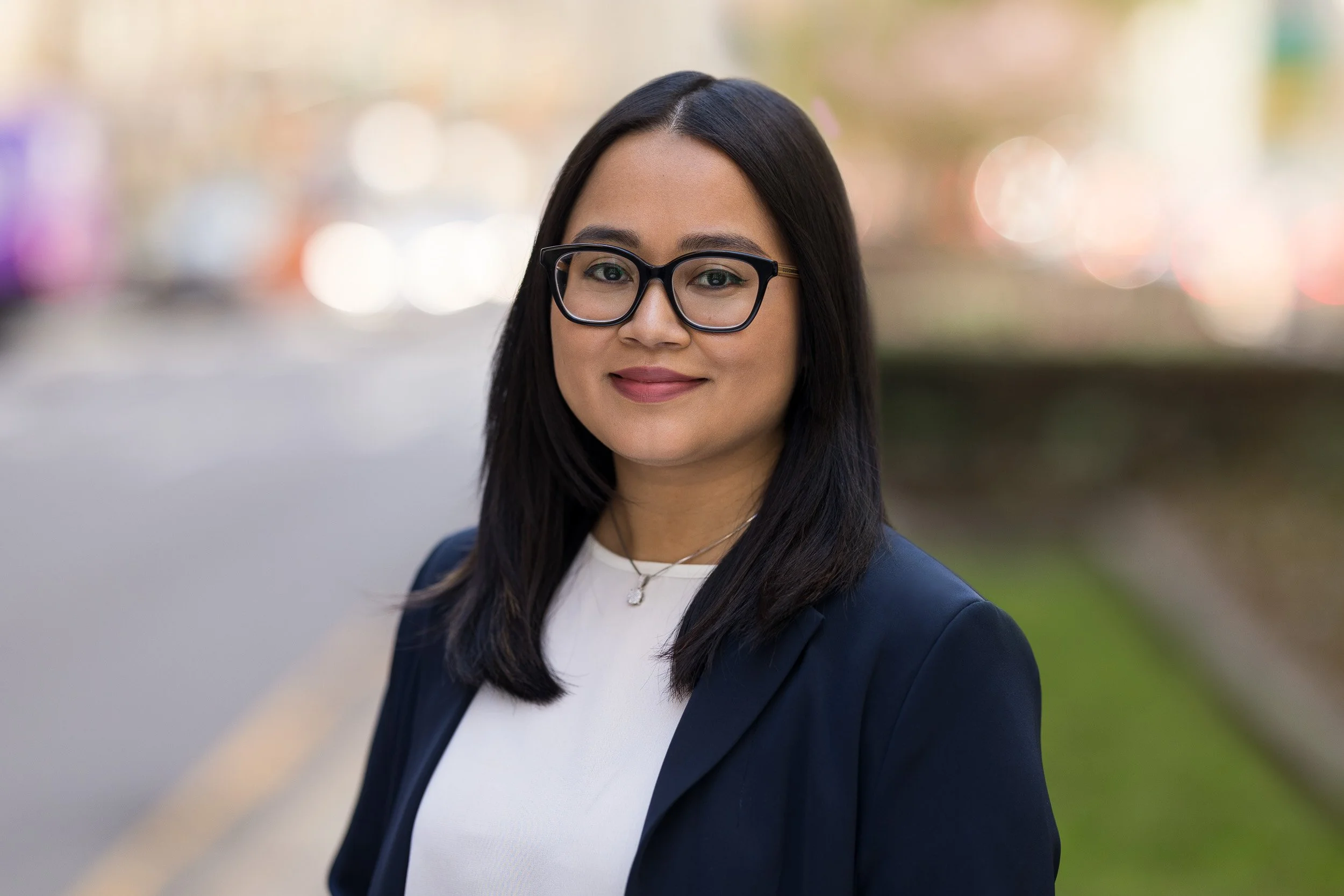 Professional headshot of female with glasses and a navy blazer outdoors in NYC