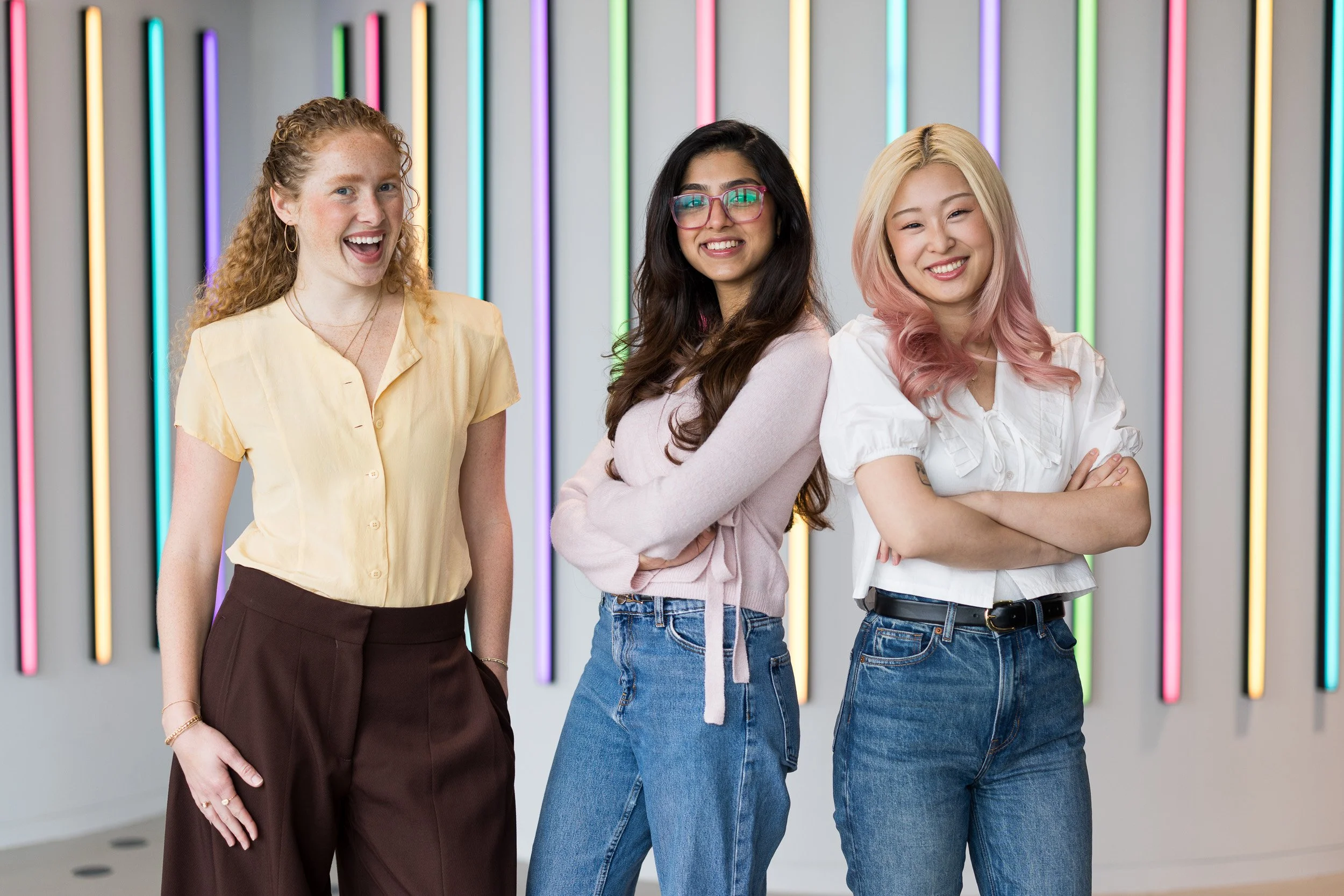 Corporate group photo of three young female employees with colorful neon lights in the background