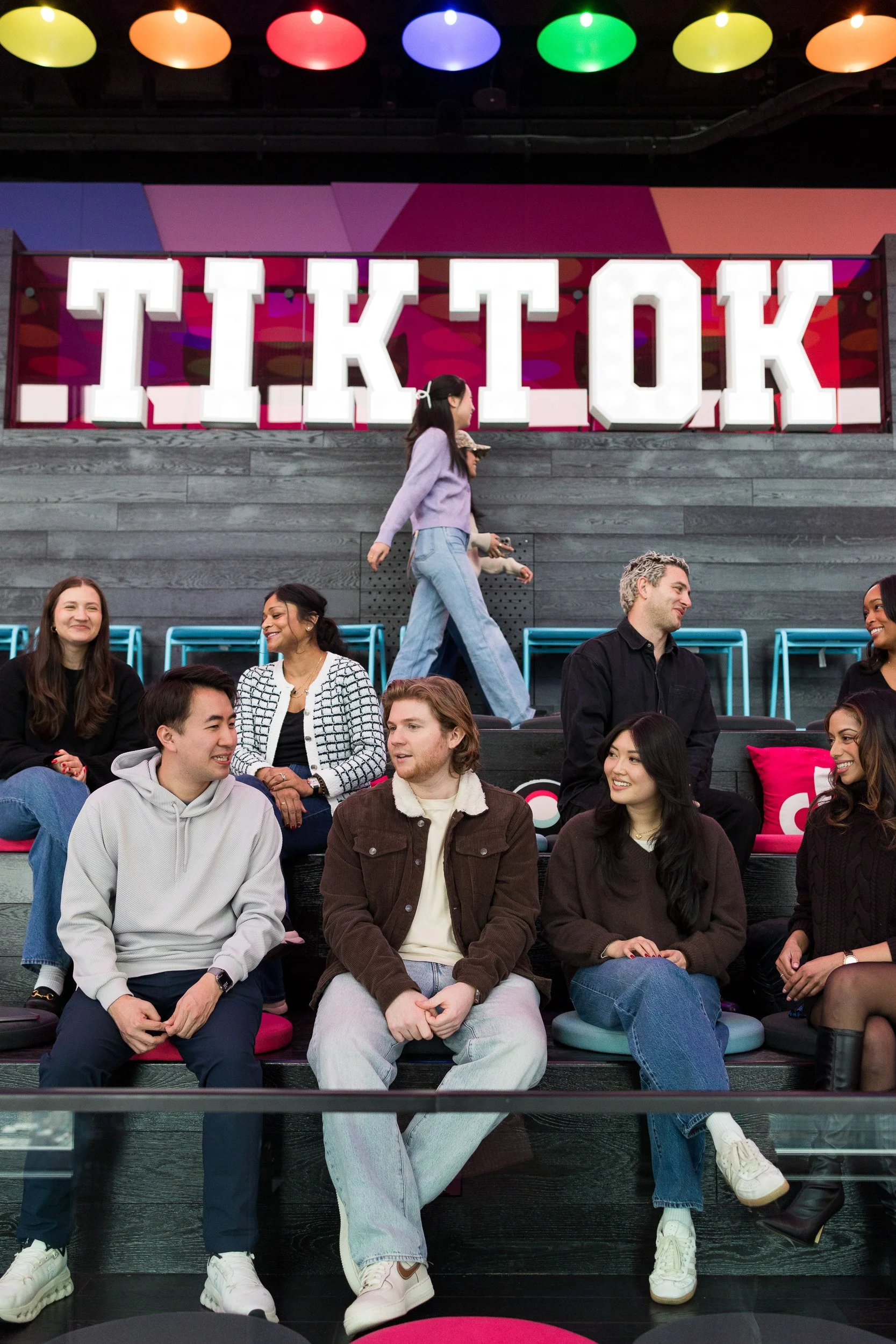 Corporate lifestyle photo of a group of young employees relaxing on a break at the TikTok NYC office with a sign that says TIKTOK in the background.
