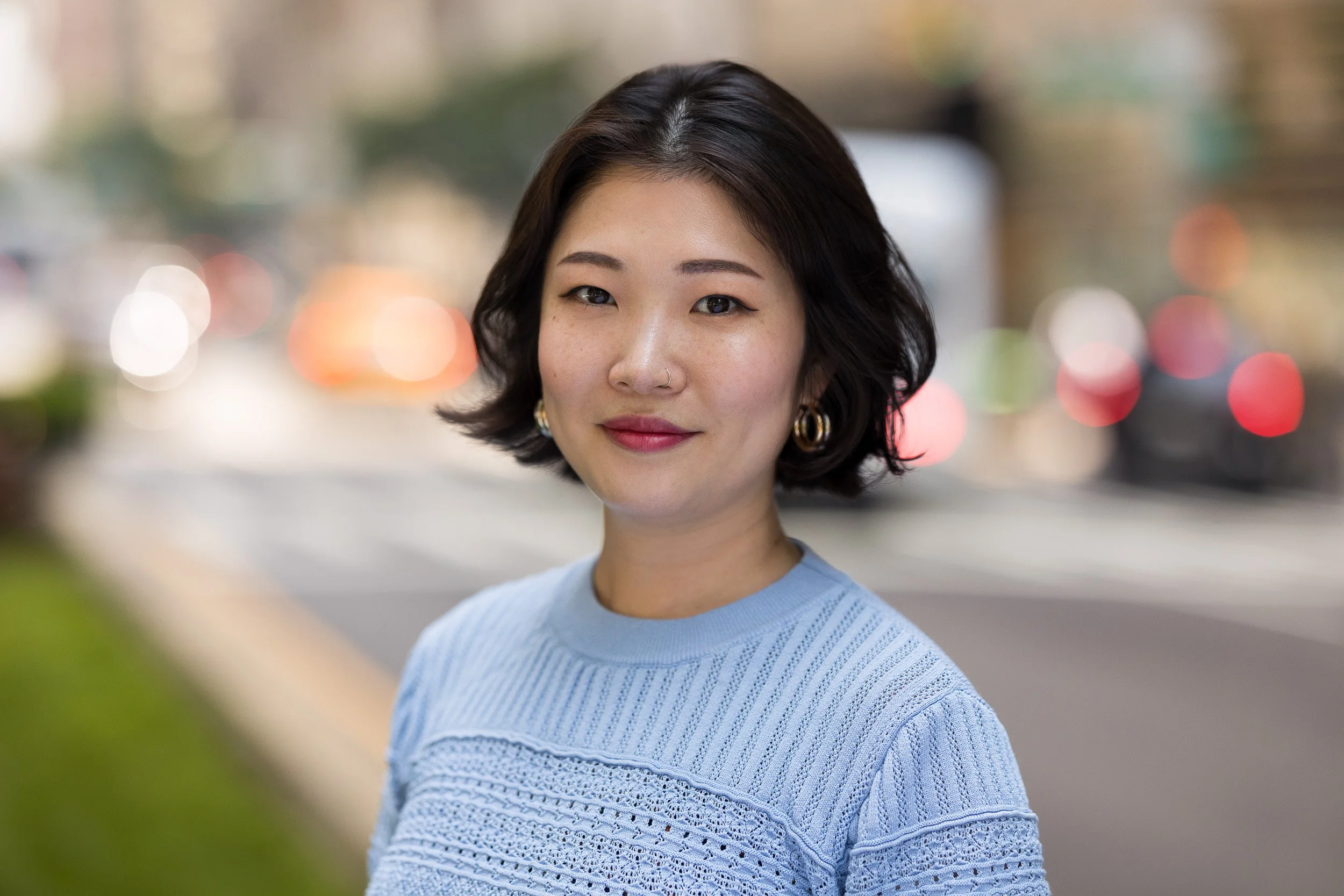 Professional headshot of a young Asian female in a blue sweater outdoors in NYC