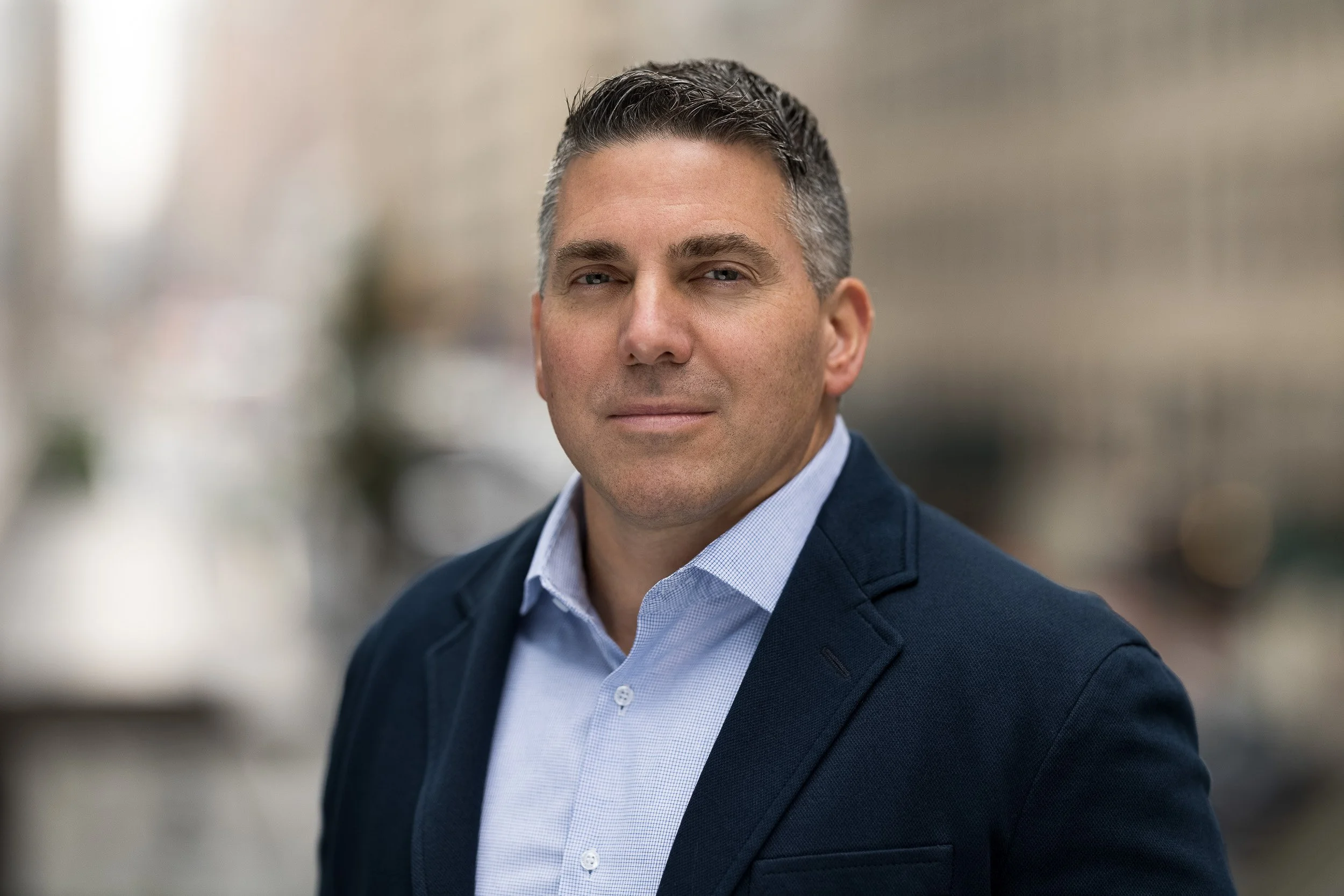 Outdoor headshot of a middle-aged male wearing a navy suit photographed outdoors with natural light in NYC