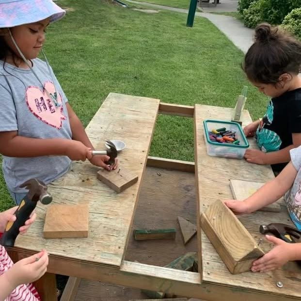 Children using hammers to build with wooden blocks at an outdoor play table