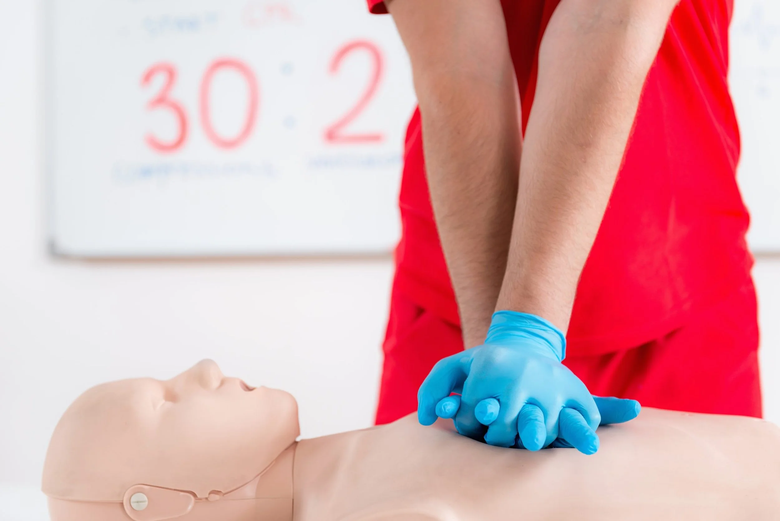 Medical professional performing CPR on a training mannequin in a classroom setting.
