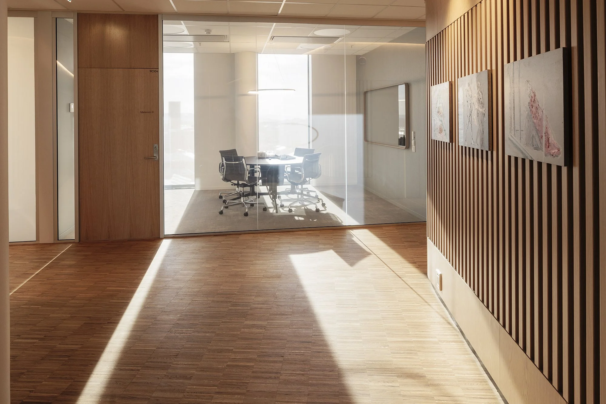 Modern office hallway with wooden flooring, glass-walled conference room, and wall art.