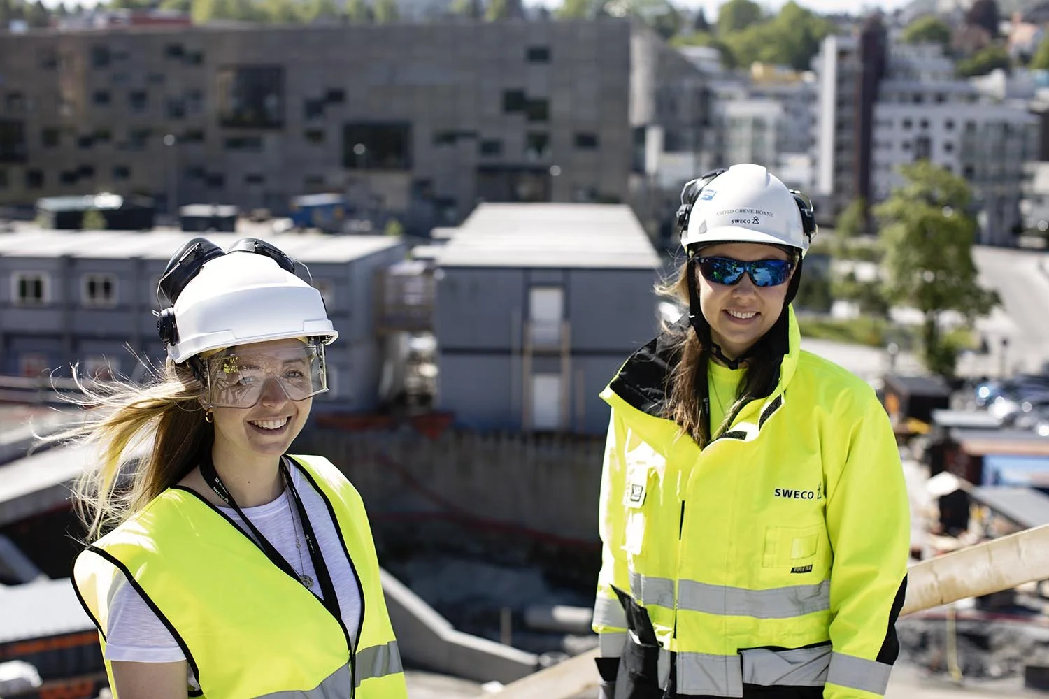 Two women wearing safety gear and high visibility vests on a construction site.