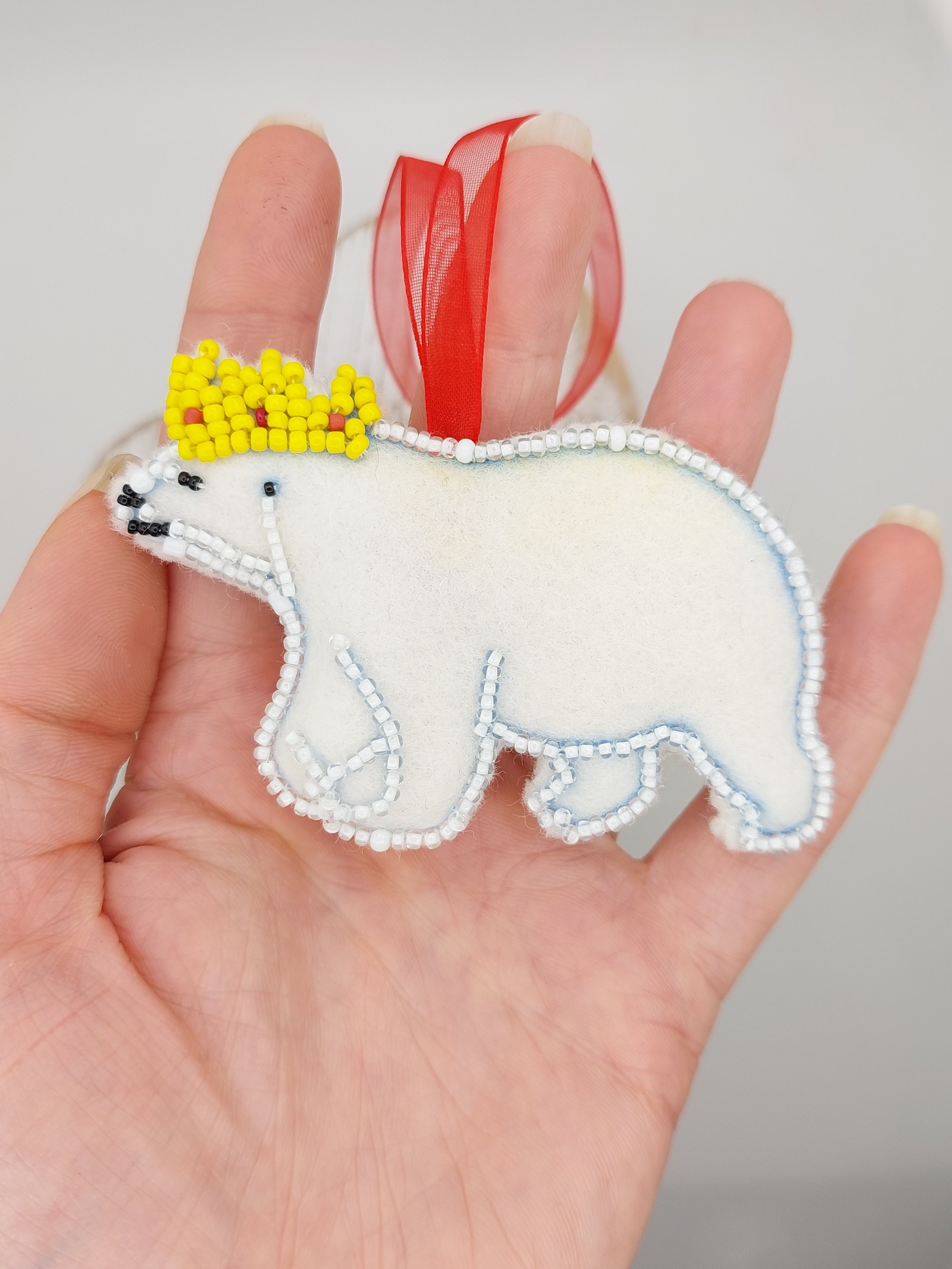 Handmade felt polar bear decoration with beaded outline and red-yellow beaded crown, red hanging ribbon – 57mm x 80mm.