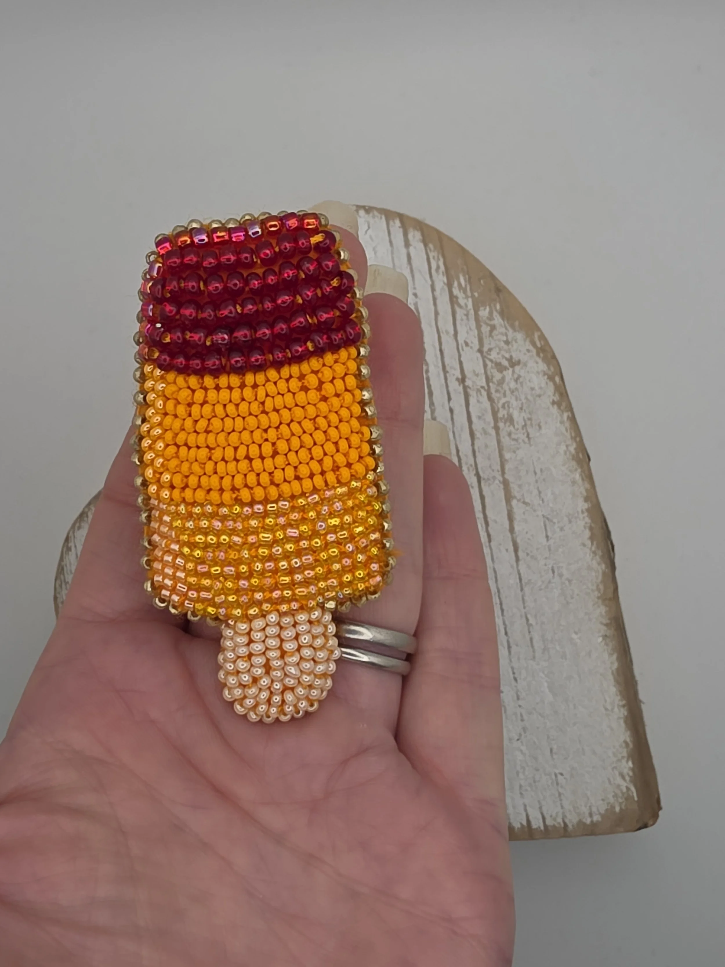 Beaded ice lolly brooch resting flat in open palm. Showcases size and hand-embroidered detail in lemon, orange, and strawberry colours.