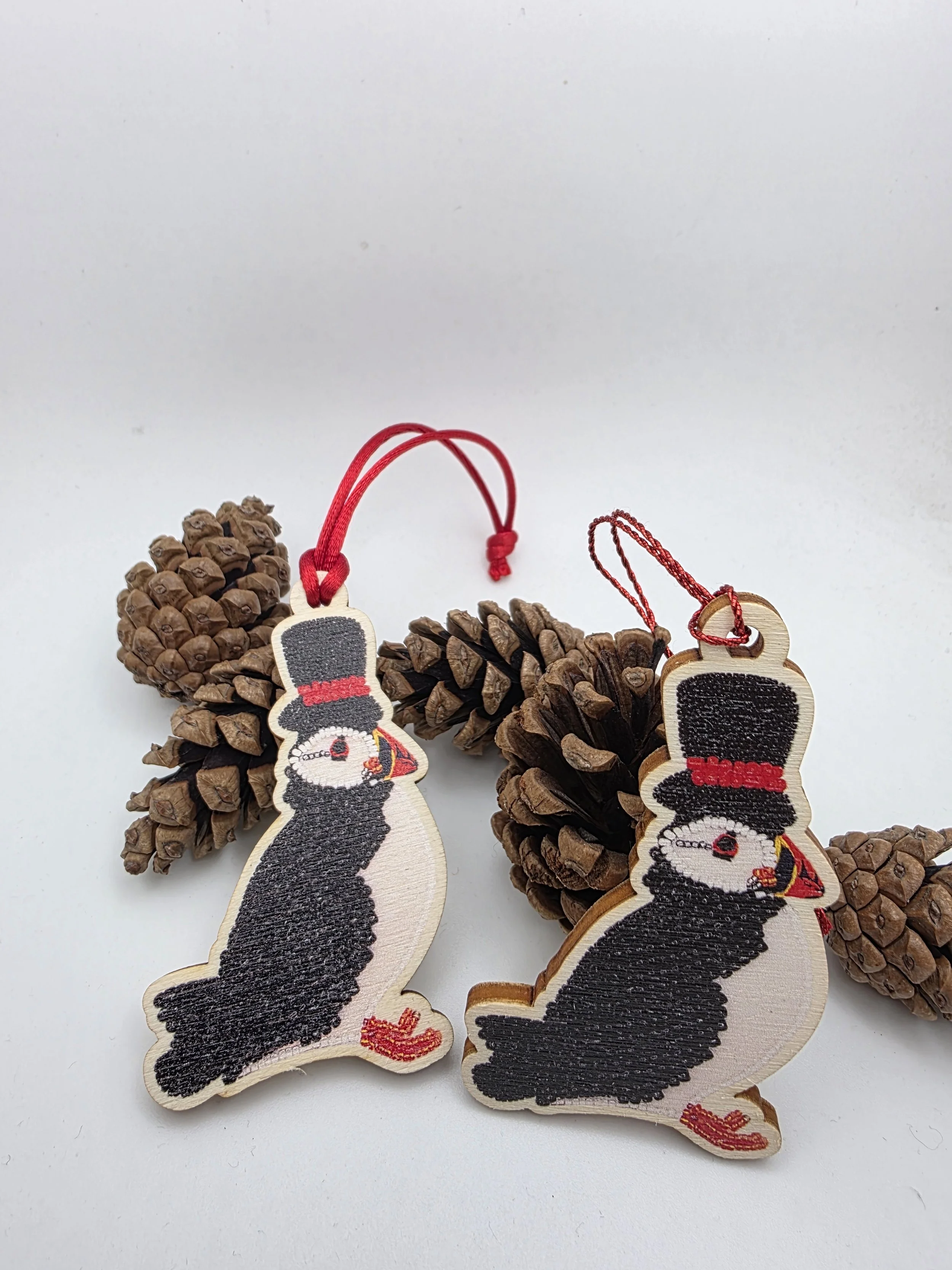 Puffin in top hat wooden decoration with choice of red hanging next to a pine cone.