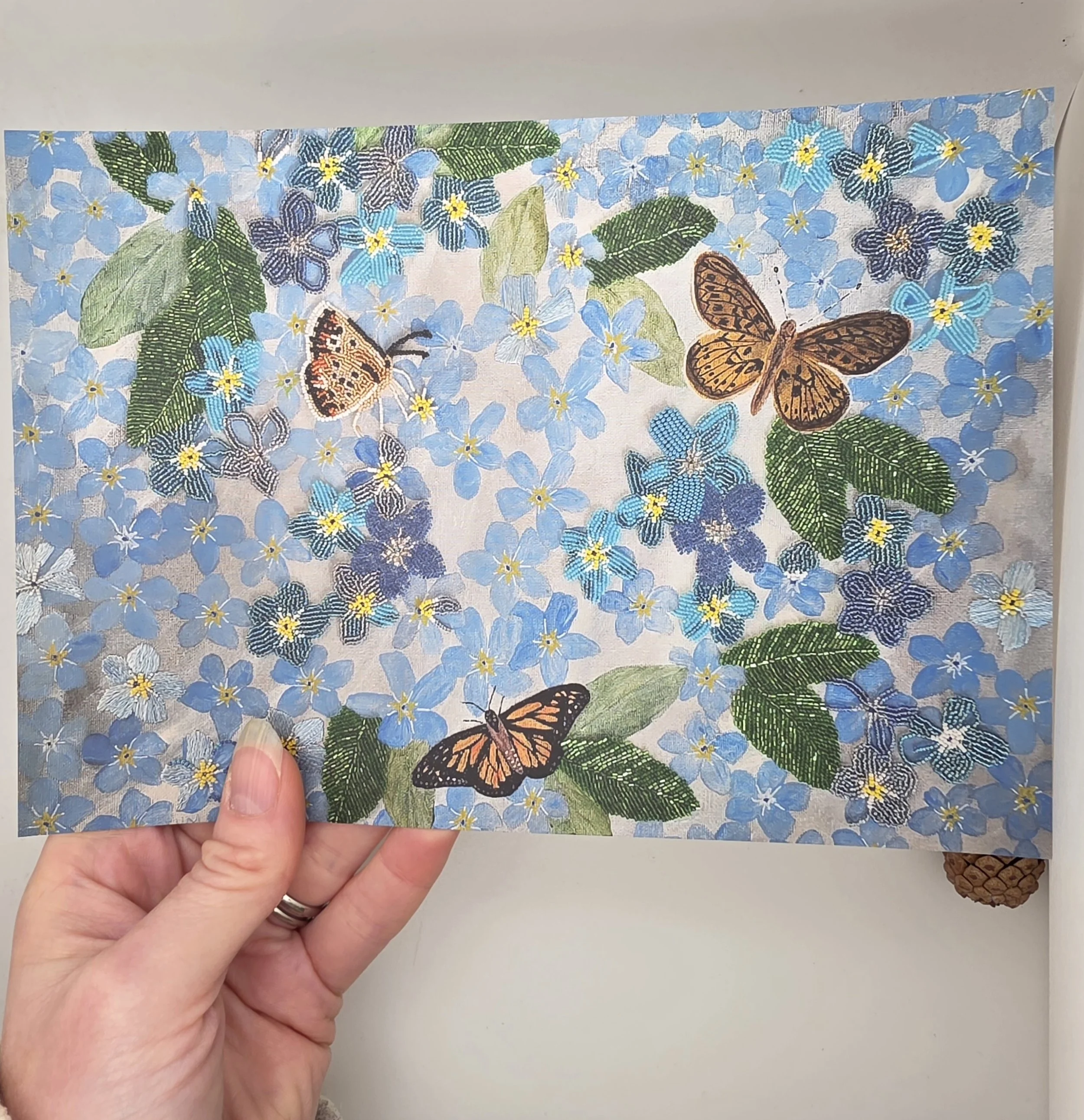 Hand holding an A5 Forget-Me-Not art print featuring delicate blue flowers and three butterflies, open edition fine art print on white background.