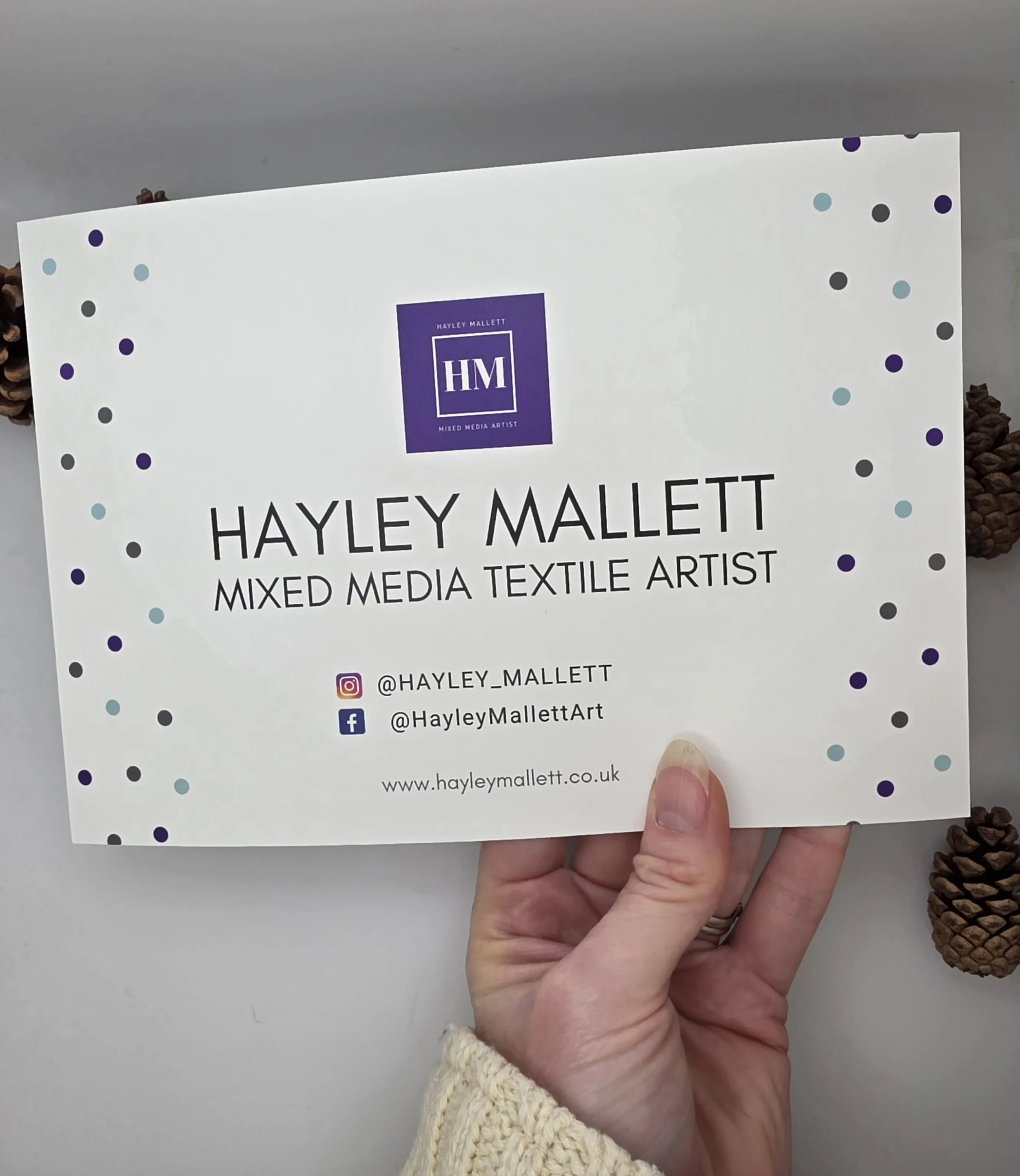 Hand holding the back of a Forget-Me-Not print with artist Hayley Mallett’s name and website visible, highlighting authentic handmade artwork.