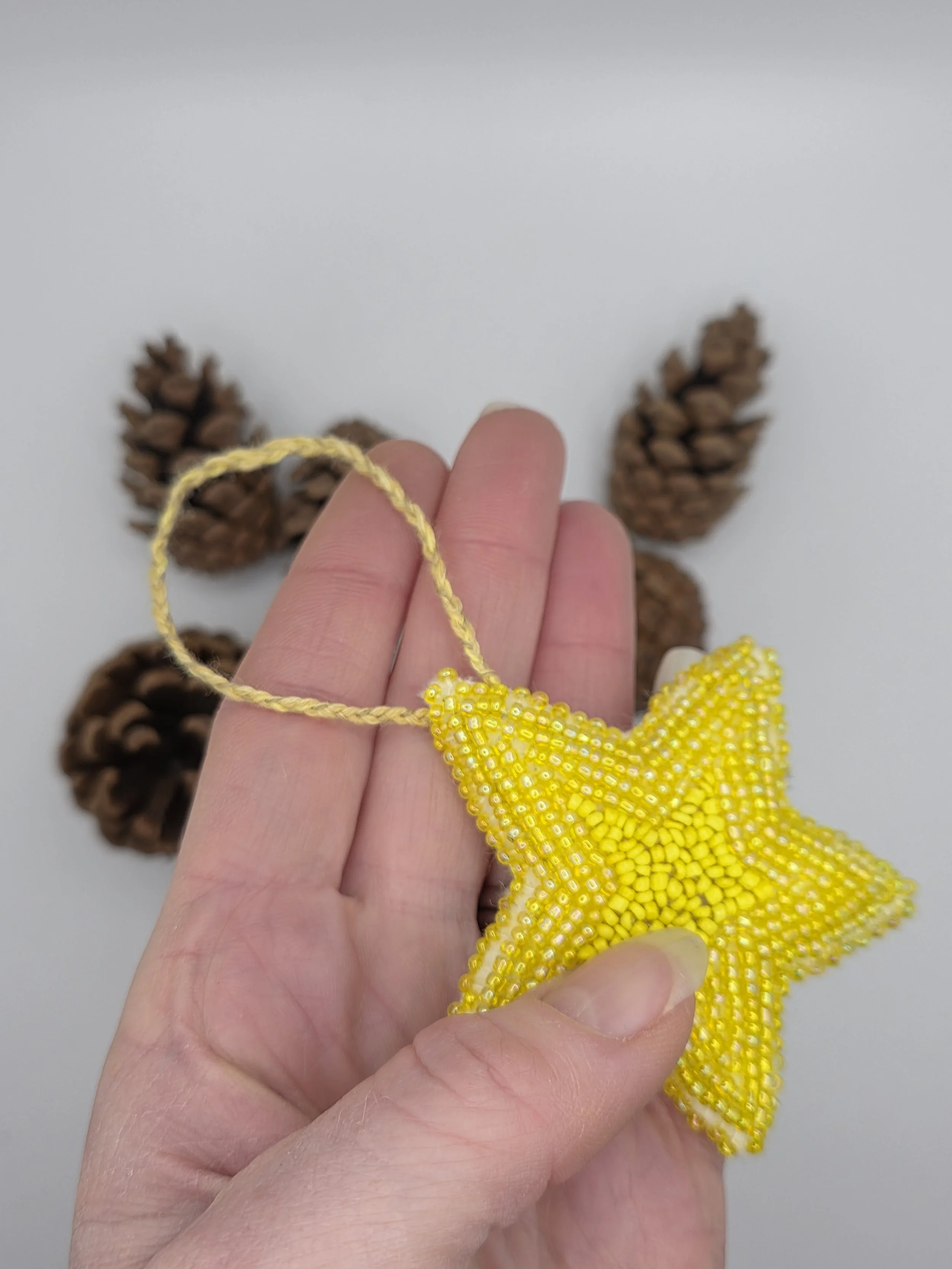 Handmade yellow beaded star decoration lying flat in a hand.