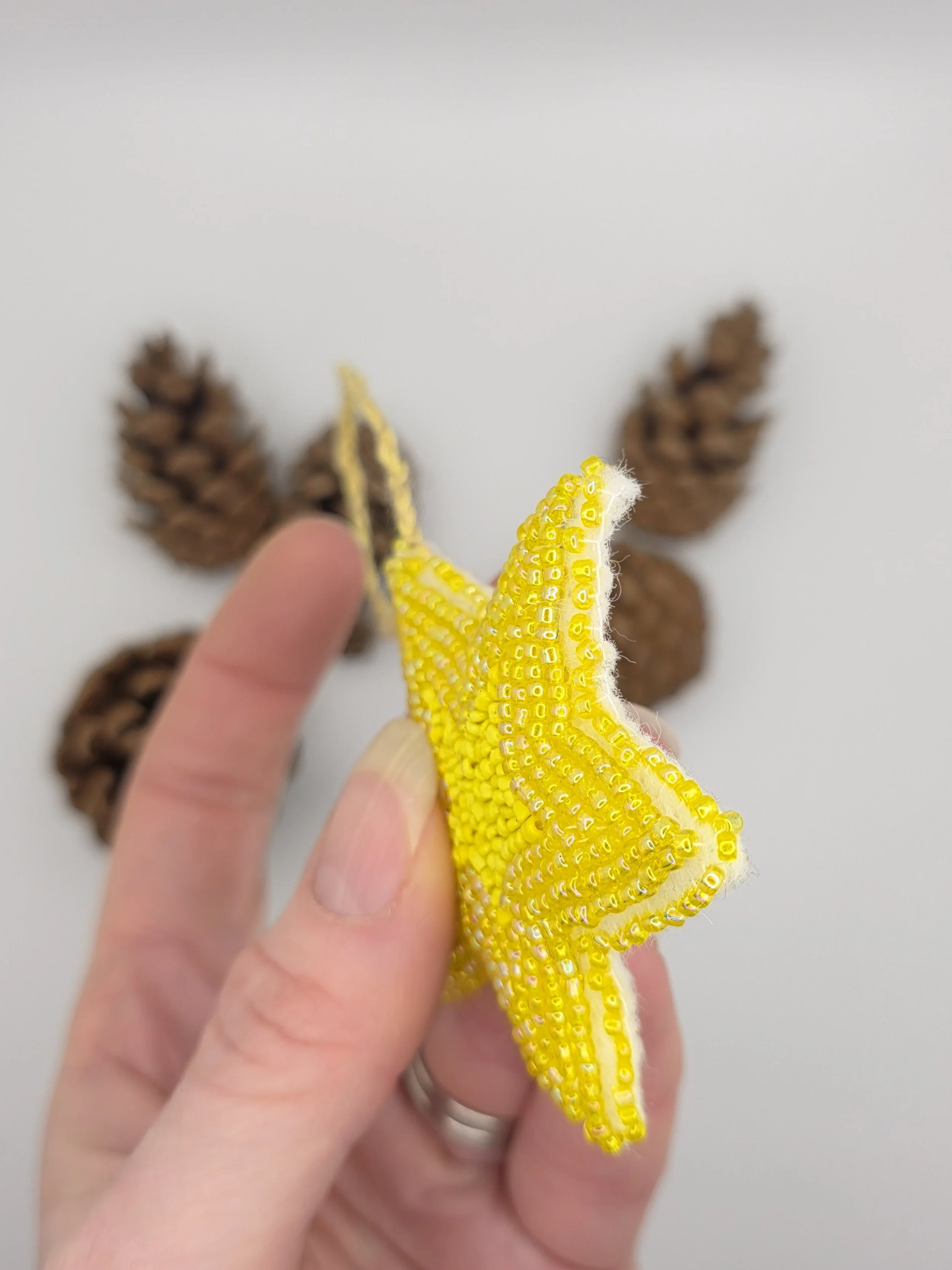 Side view of a handmade yellow beaded star decoration held in a hand.