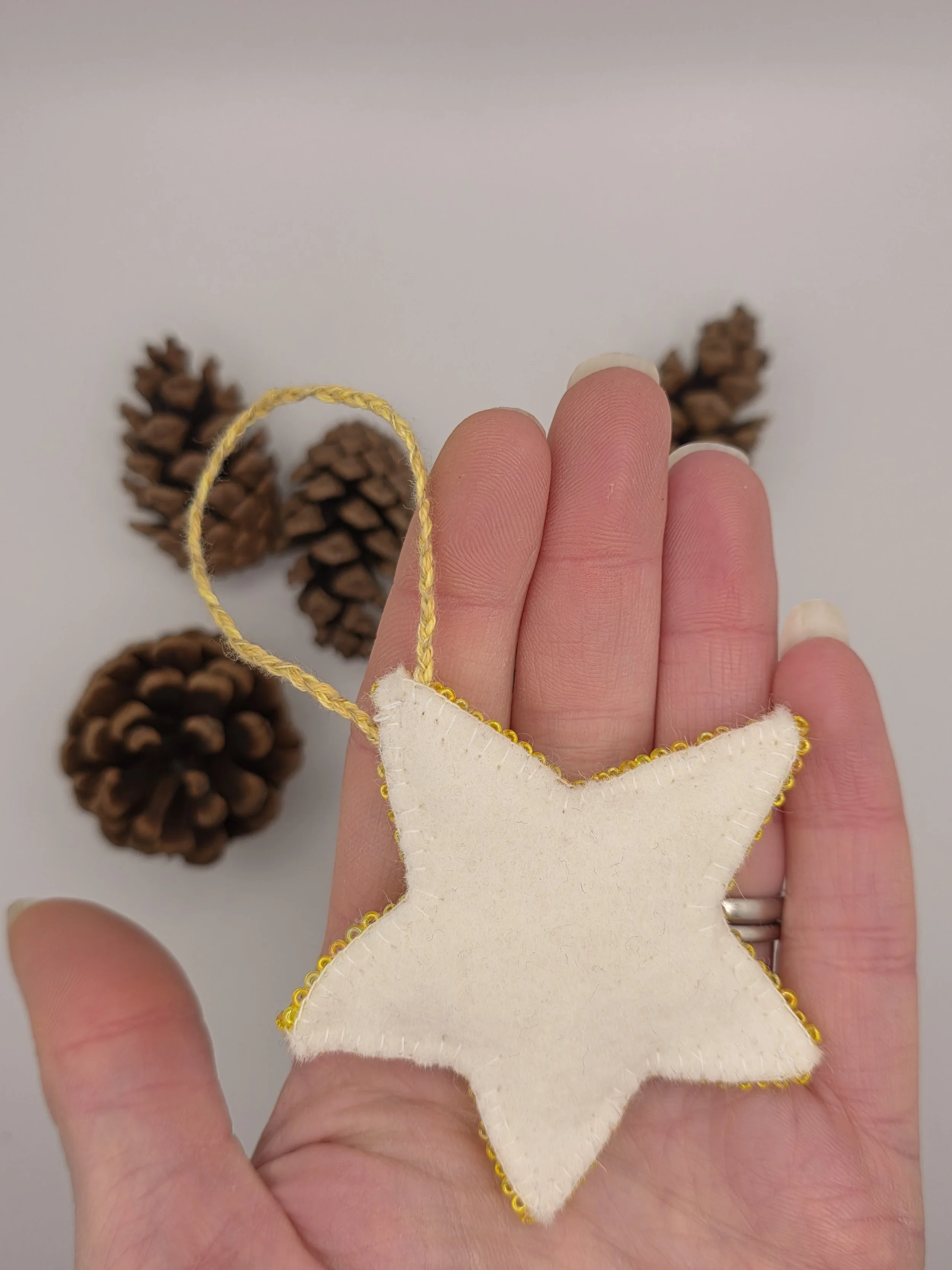Back of a handmade yellow beaded star decoration lying flat in a hand.