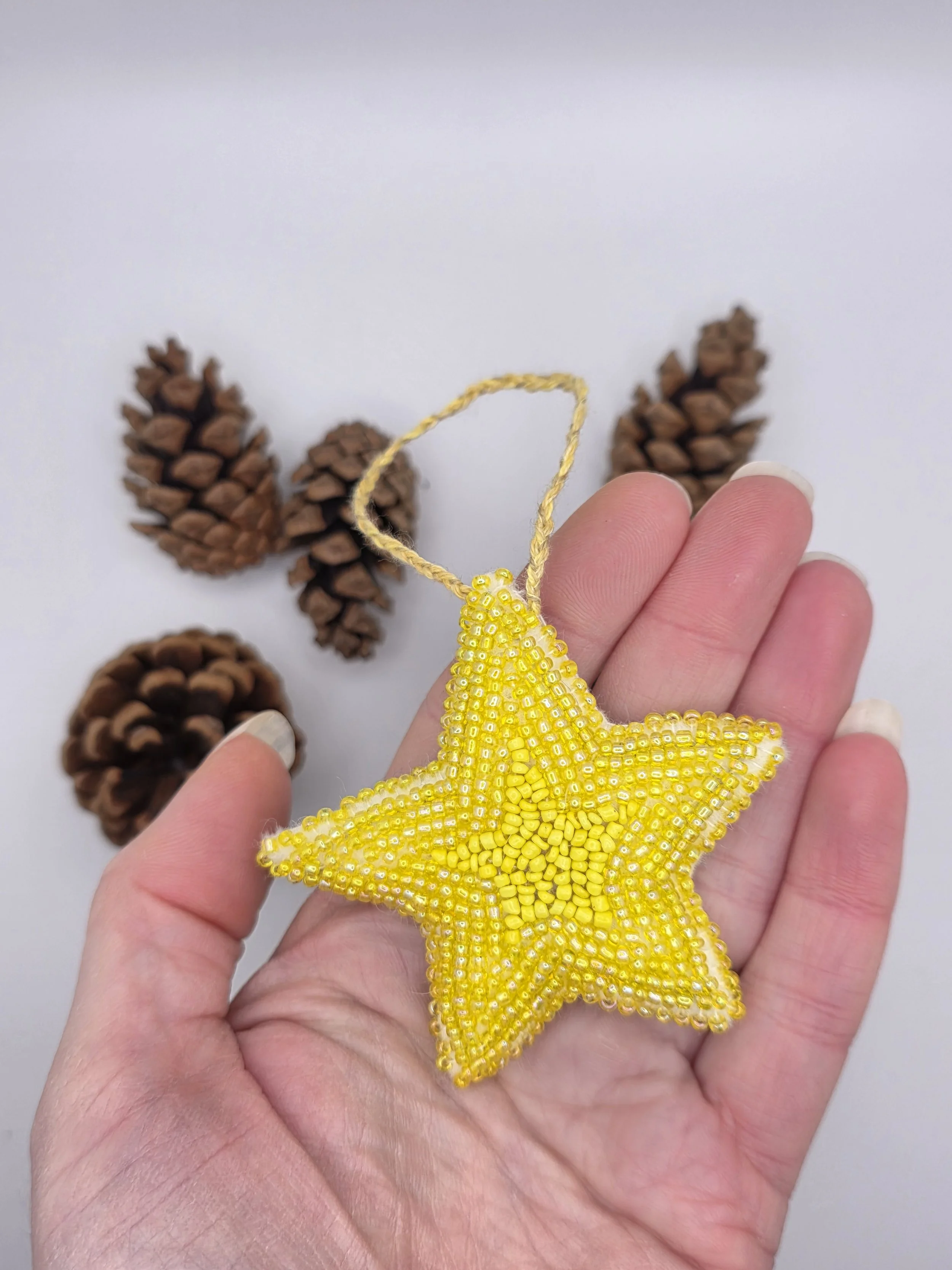 Handmade yellow bead-embroidered star lying flat in an open hand against a neutral background.