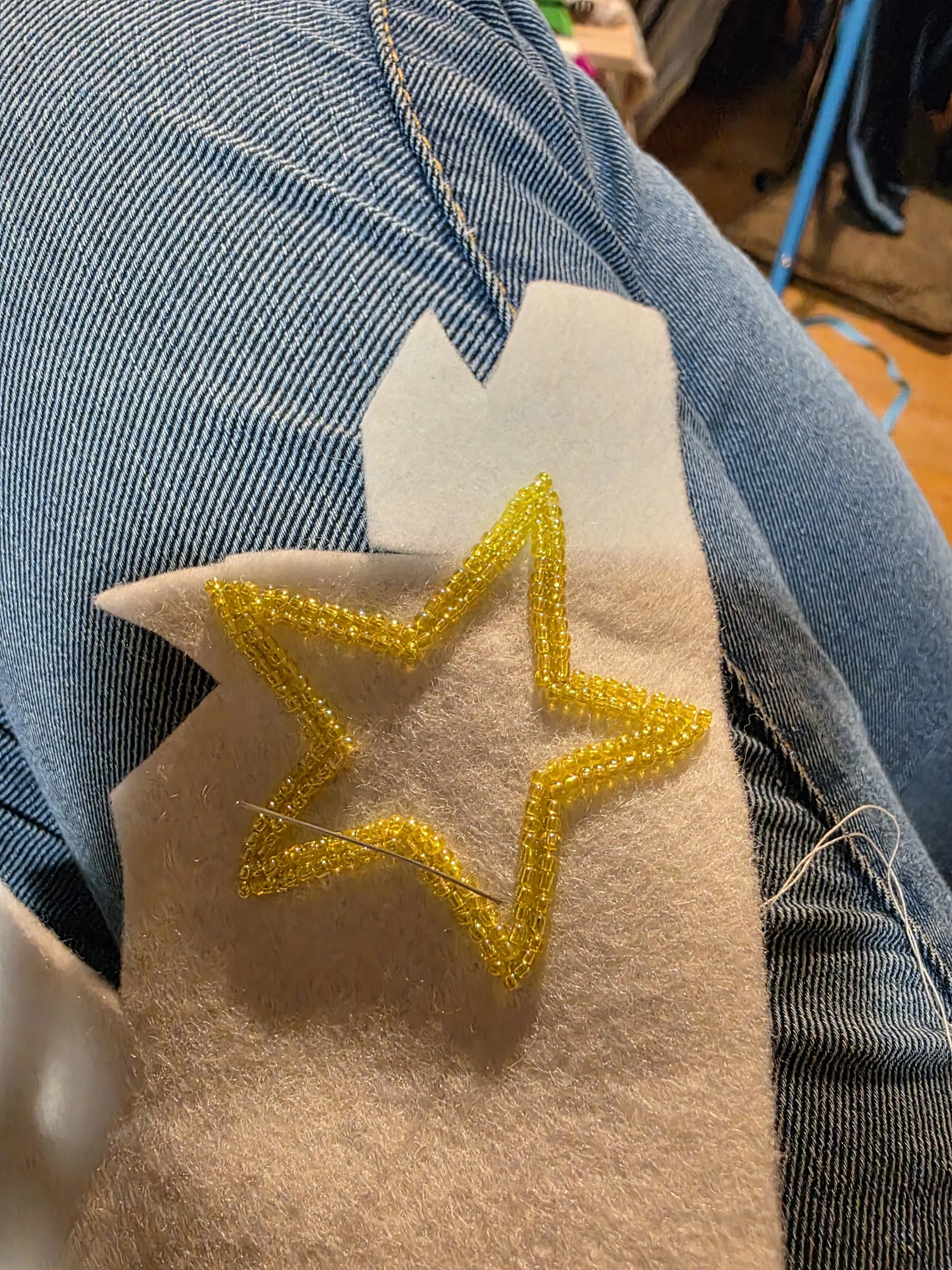 Work in progress of a handmade yellow beaded star decoration resting on jeans.