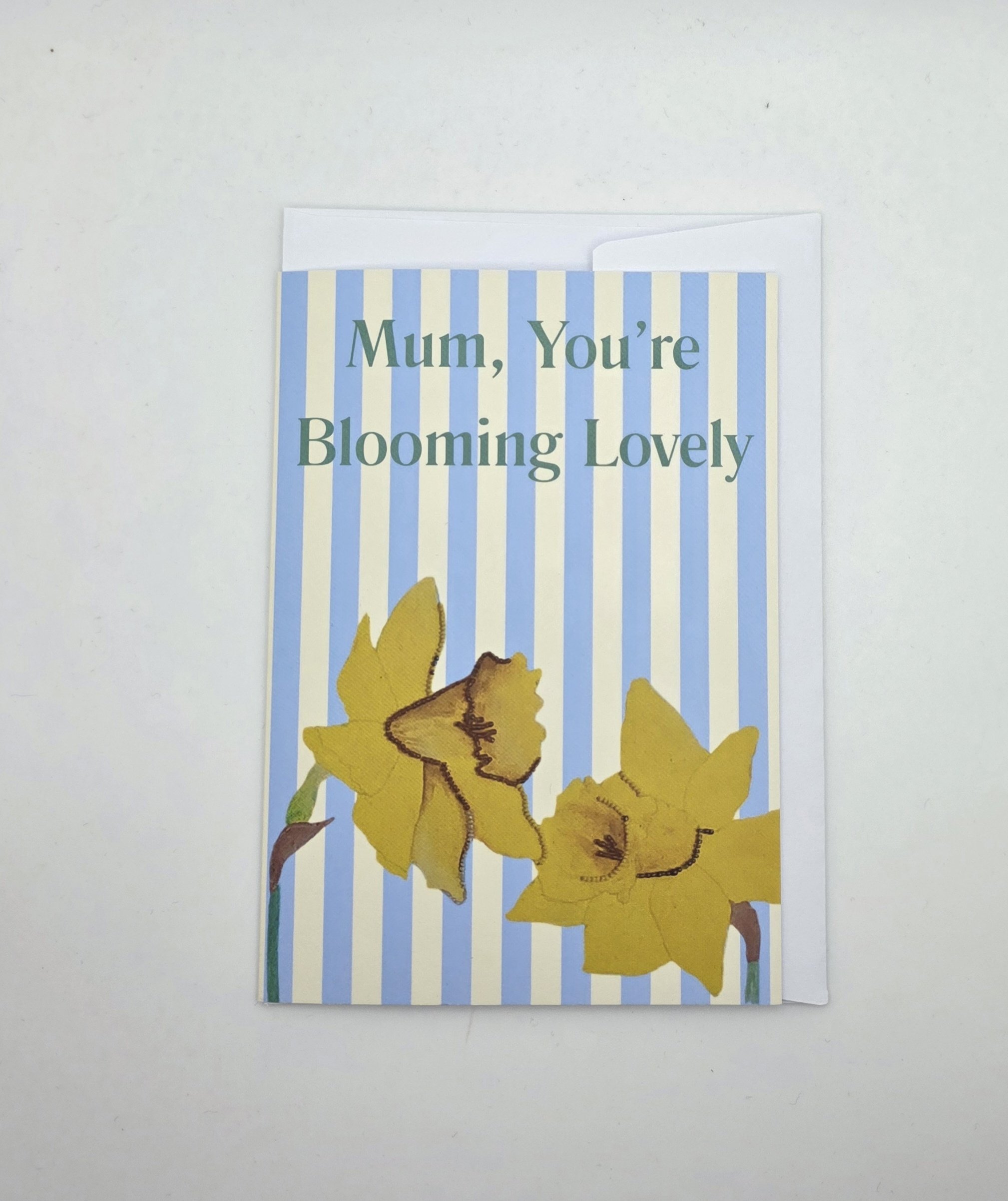 Mum, You’re Blooming Lovely’ daffodil Mother’s Day card on white background, A6 portrait with blue and cream stripes.