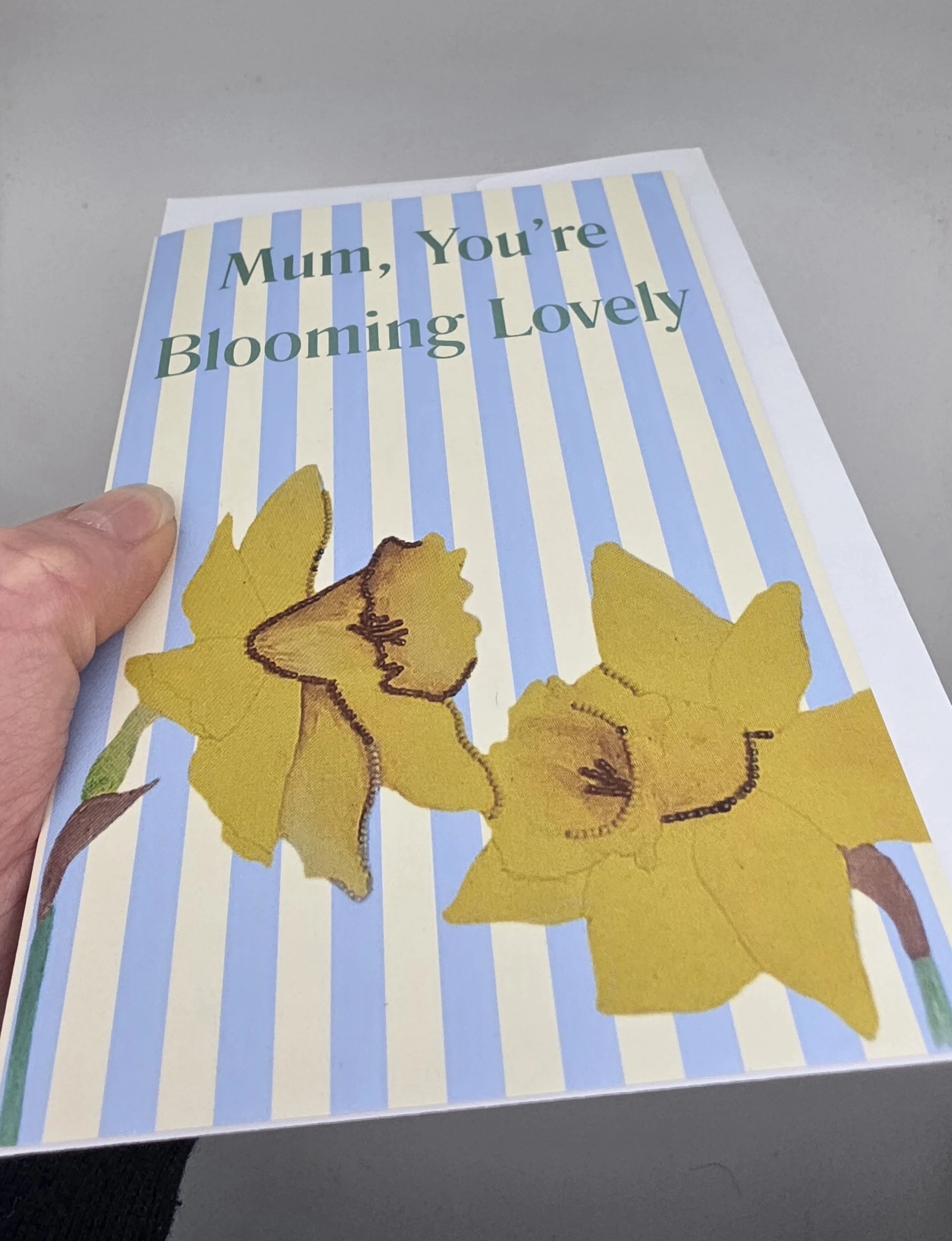 Handmade-inspired A6 Mother’s Day card with daffodils and striped background, reading ‘Mum, You’re Blooming Lovely’.