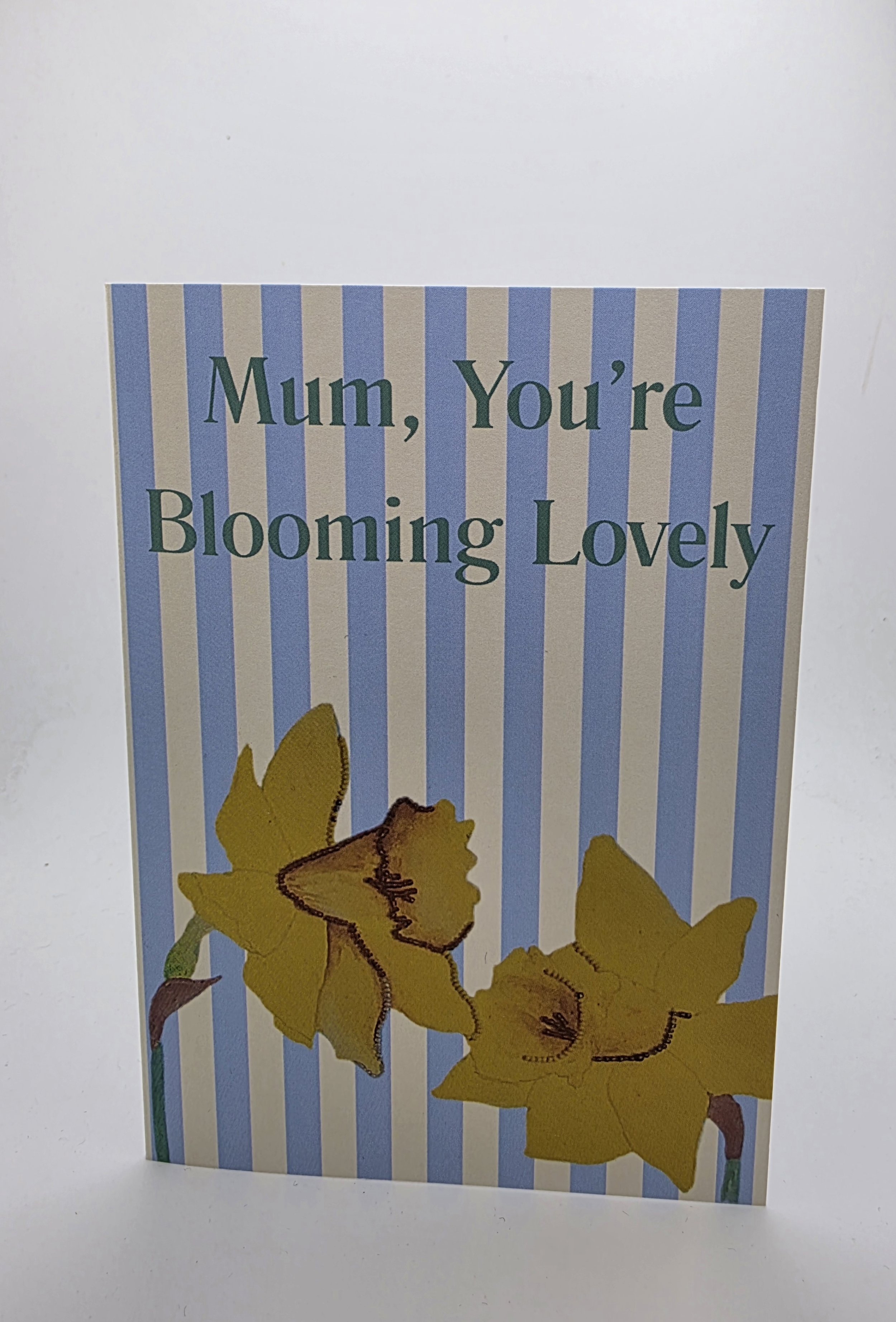 ‘Mum, You’re Blooming Lovely’ floral Mother’s Day card standing on white background, A6 portrait with daffodil design.