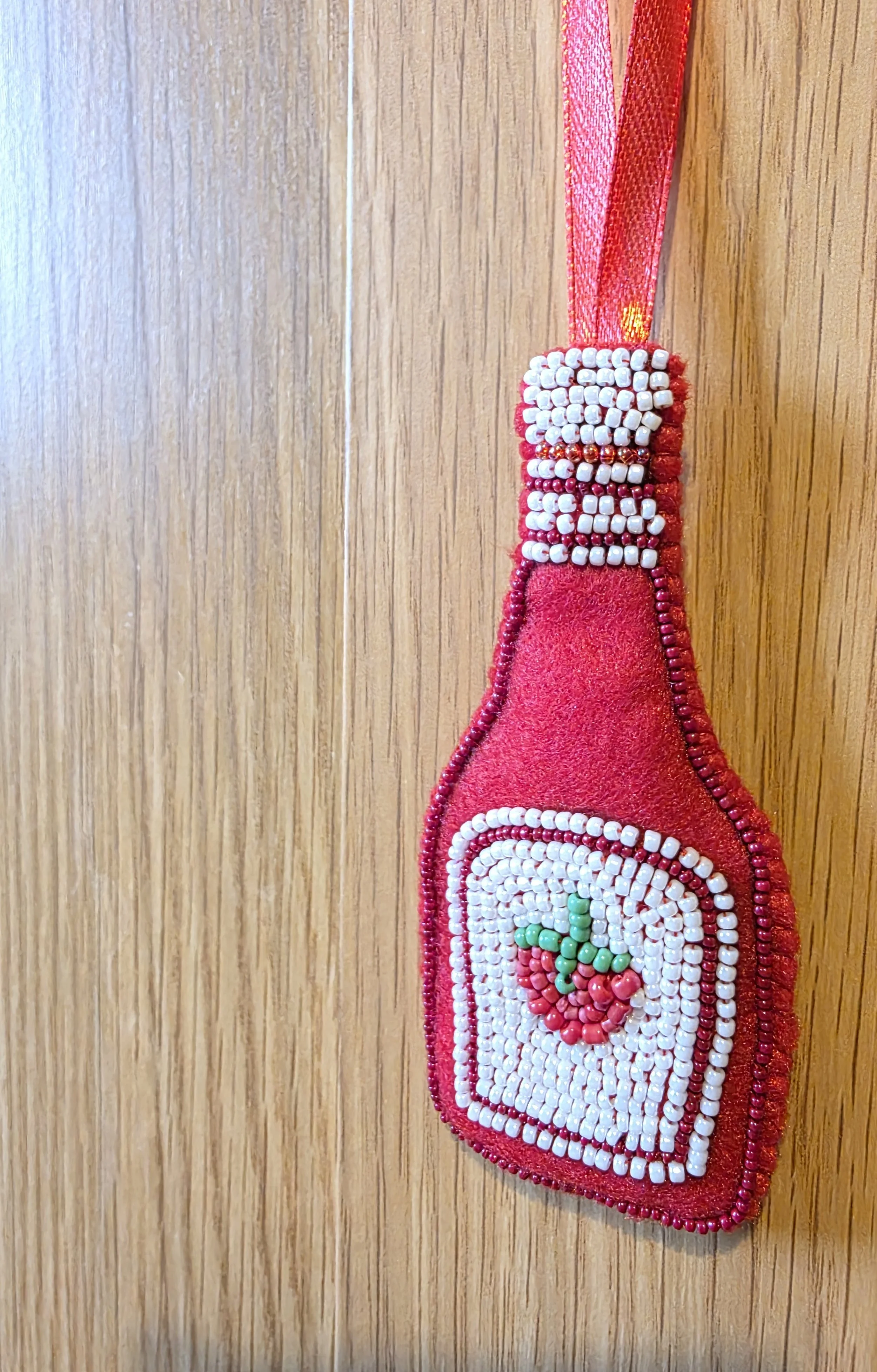 Handmade beaded tomato ketchup Christmas decoration hanging against a wooden cupboard