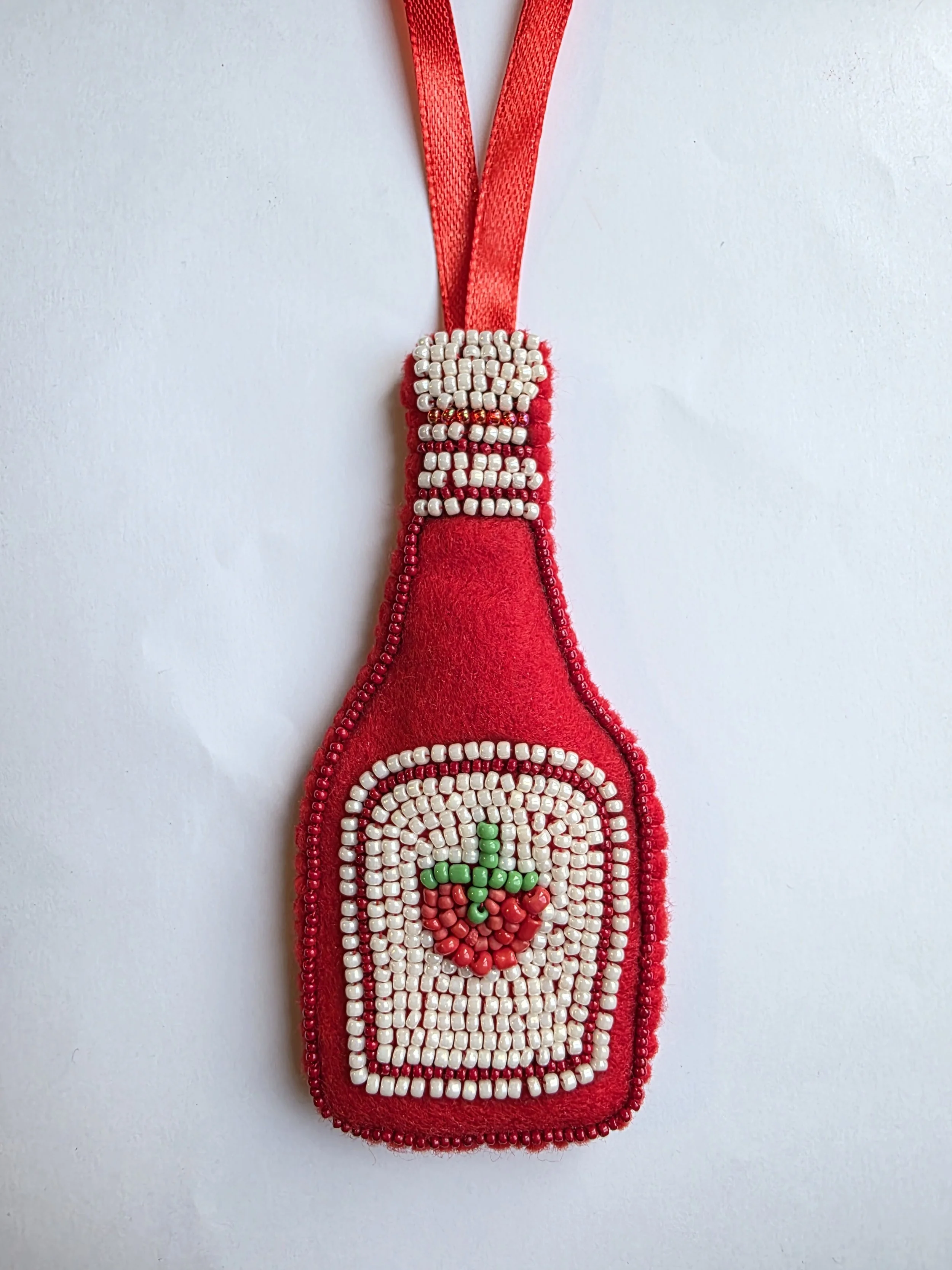 Handmade beaded tomato ketchup Christmas decoration laid flat on a white background