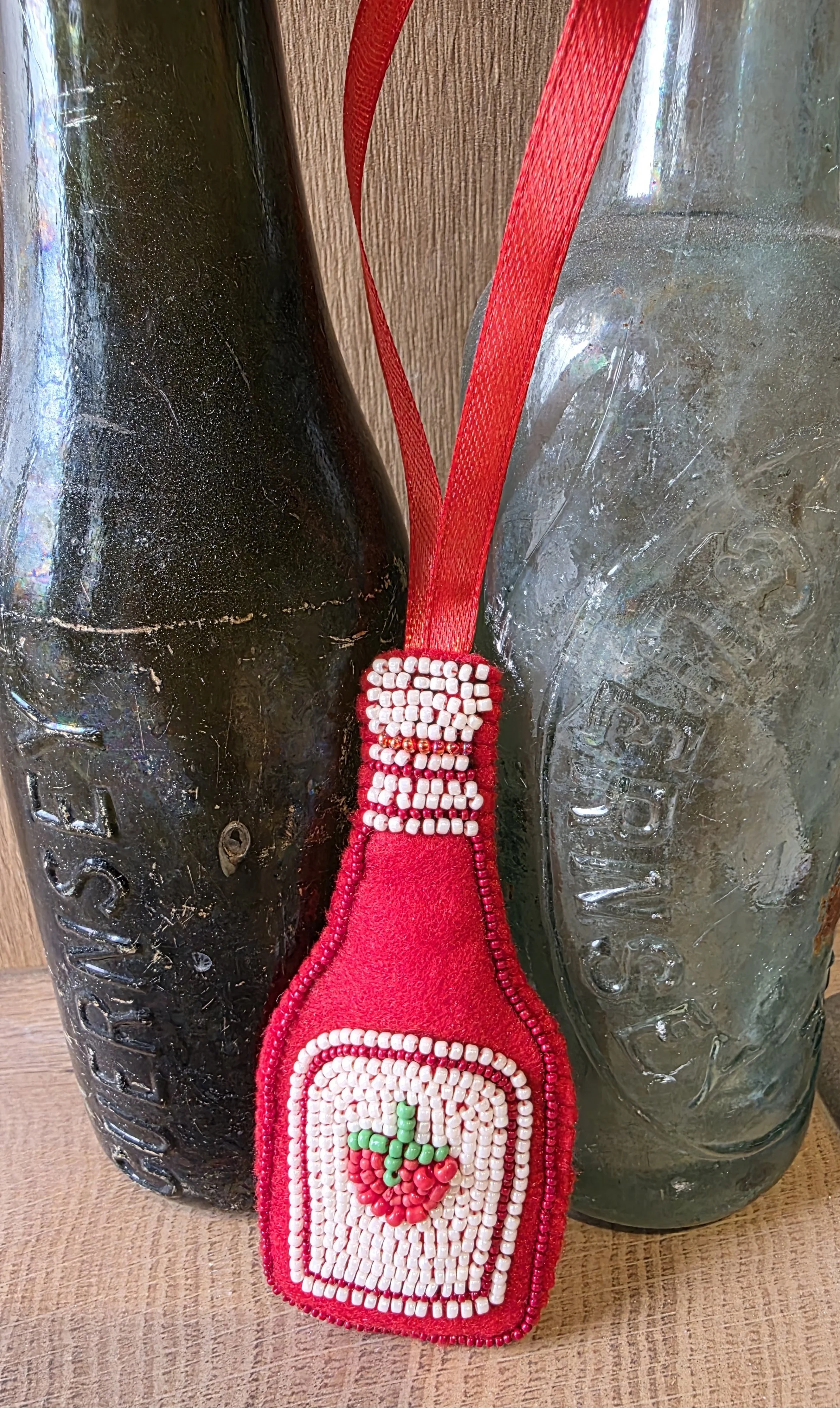 Handmade beaded tomato ketchup Christmas decoration leaning against antique glass bottles