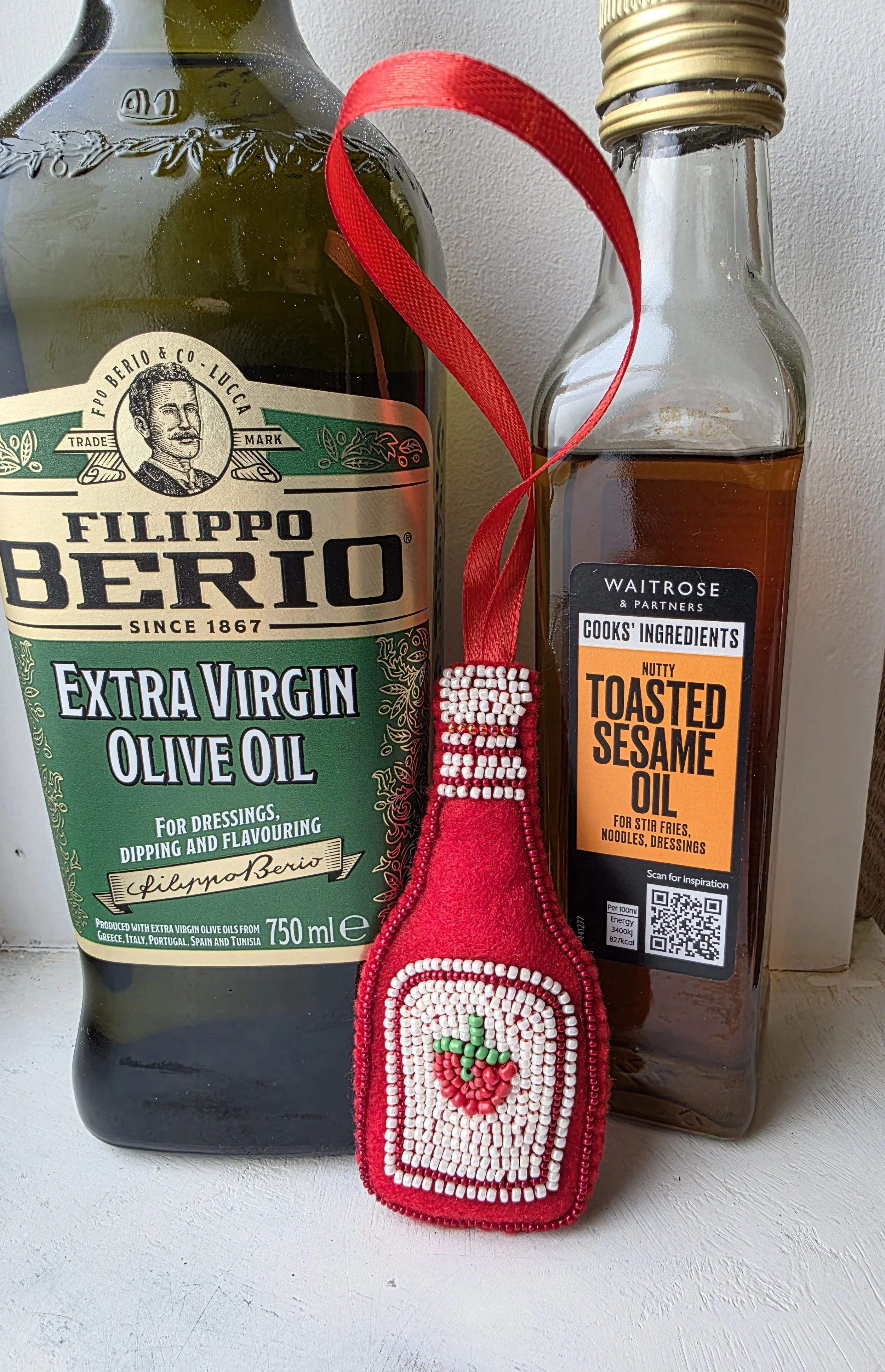 Handmade beaded tomato ketchup Christmas decoration leaning against bottles of olive and sesame oil