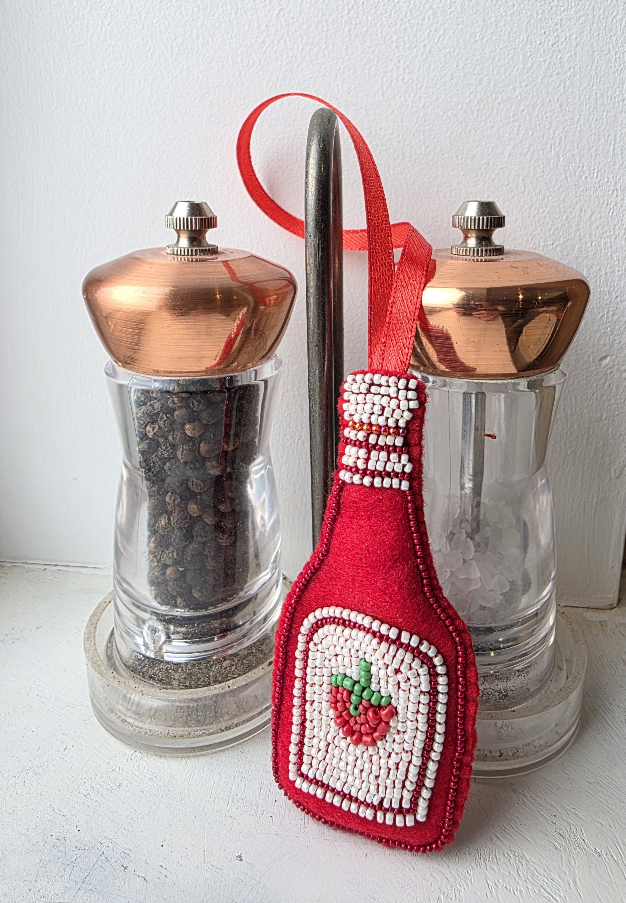 Handmade beaded tomato ketchup Christmas decoration leaning against salt and pepper grinders