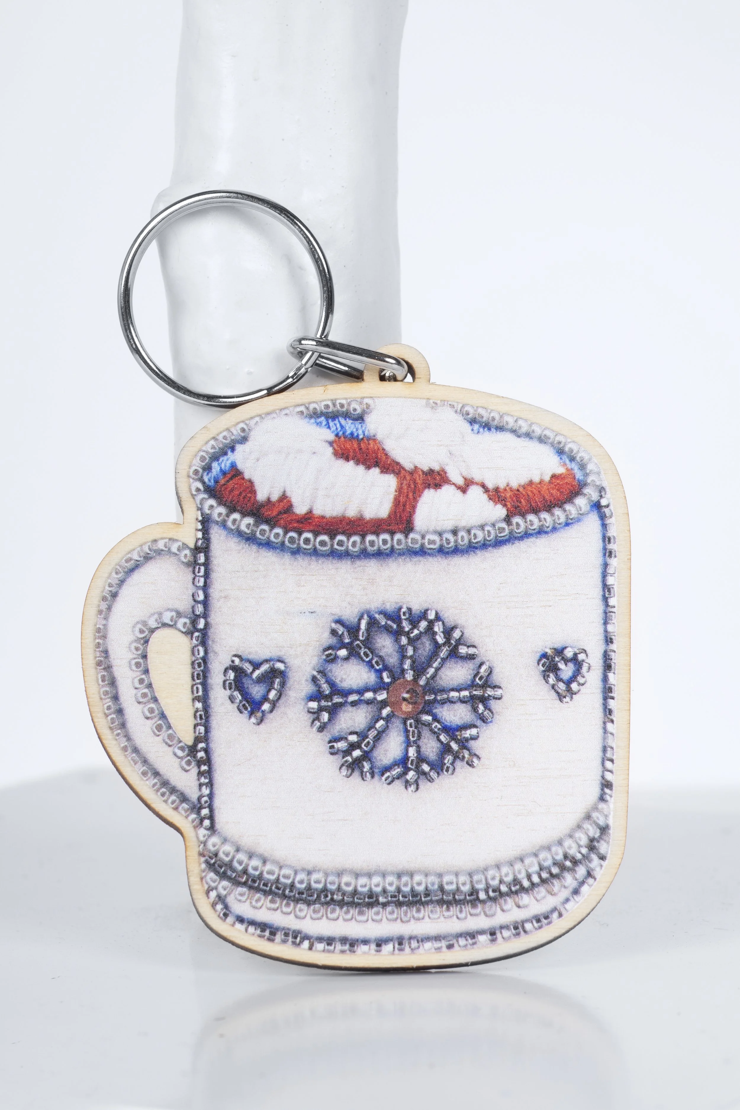 Wooden hot chocolate keyring illustrated by Hayley Mallett, displayed standing against a small white tree-trunk prop.