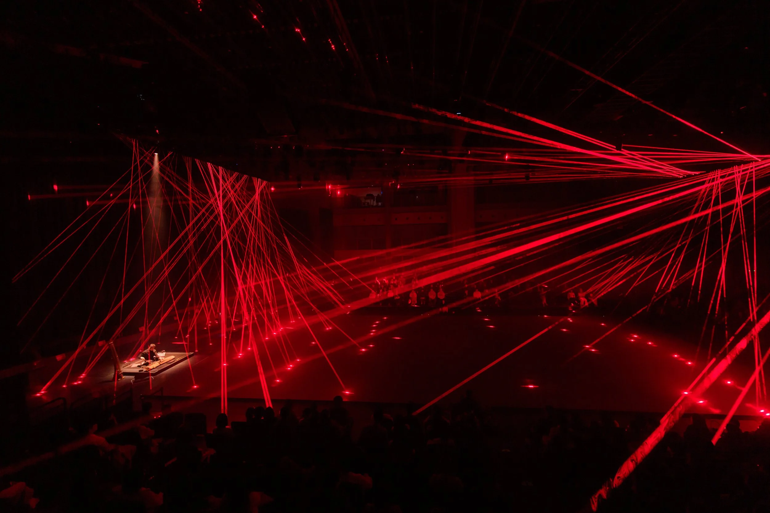Red laser light show in a dark indoor venue with audience
