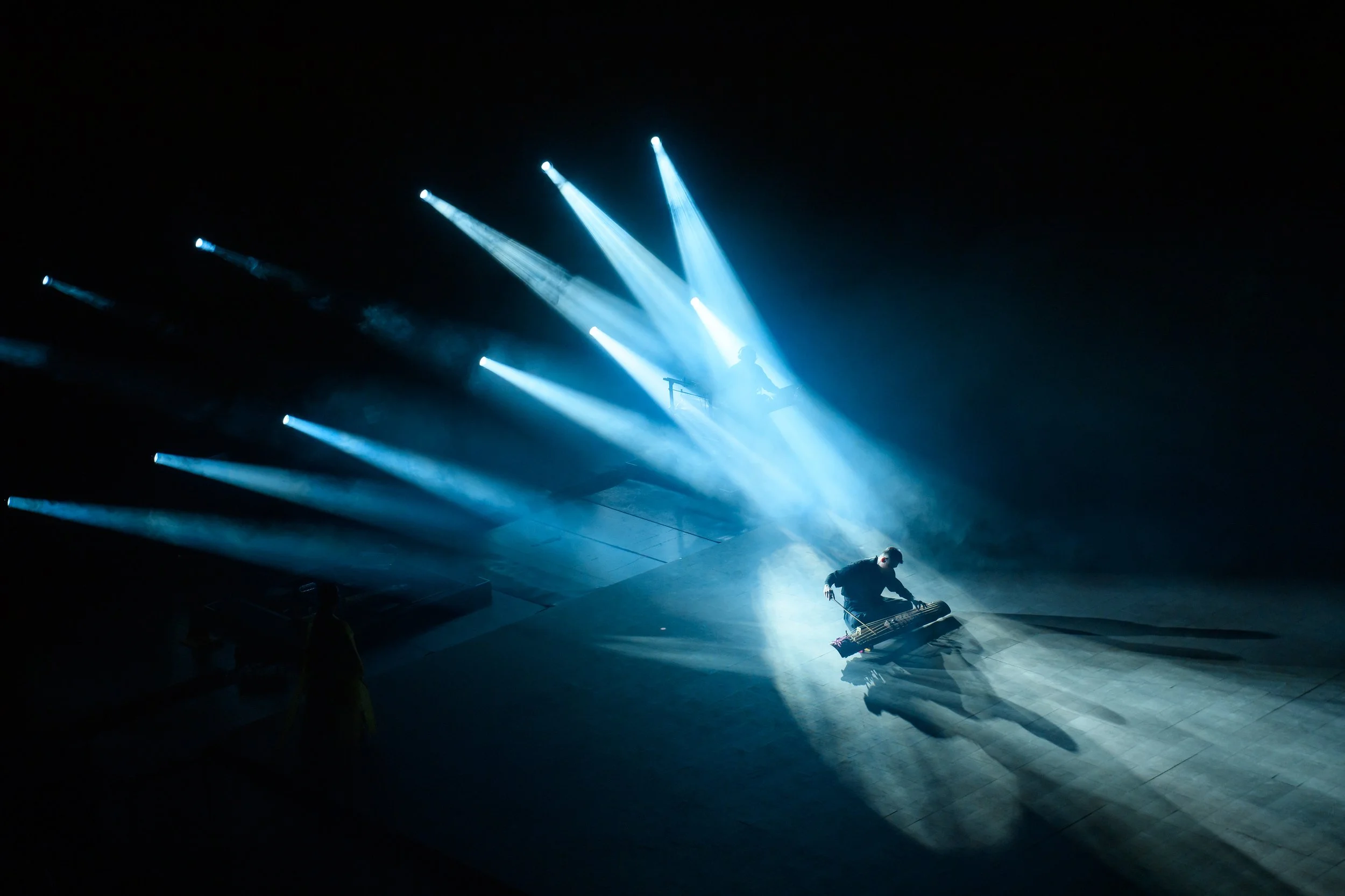 A person performing on stage with dramatic blue lighting and shadows.