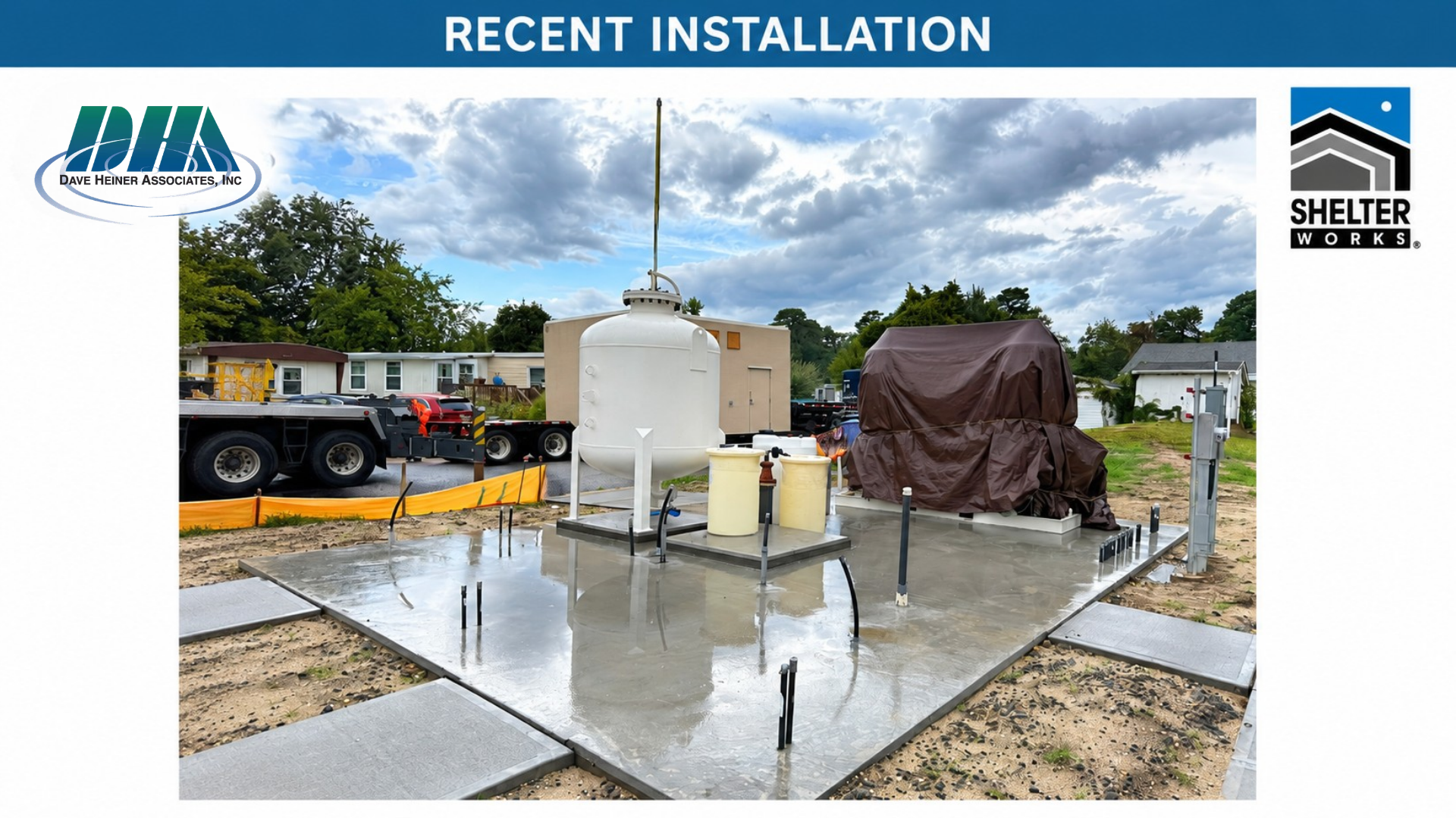 Construction site showing a recently installed foundation for a building, with concrete, pipes, and equipment, under a cloudy sky.
