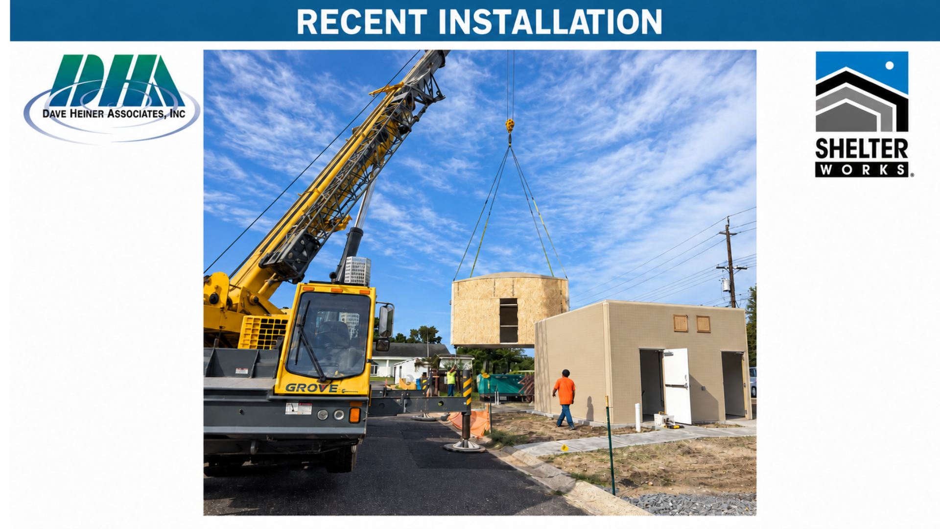 A yellow crane lifting a wooden structure at a construction site with a small beige building nearby, under a partly cloudy sky.