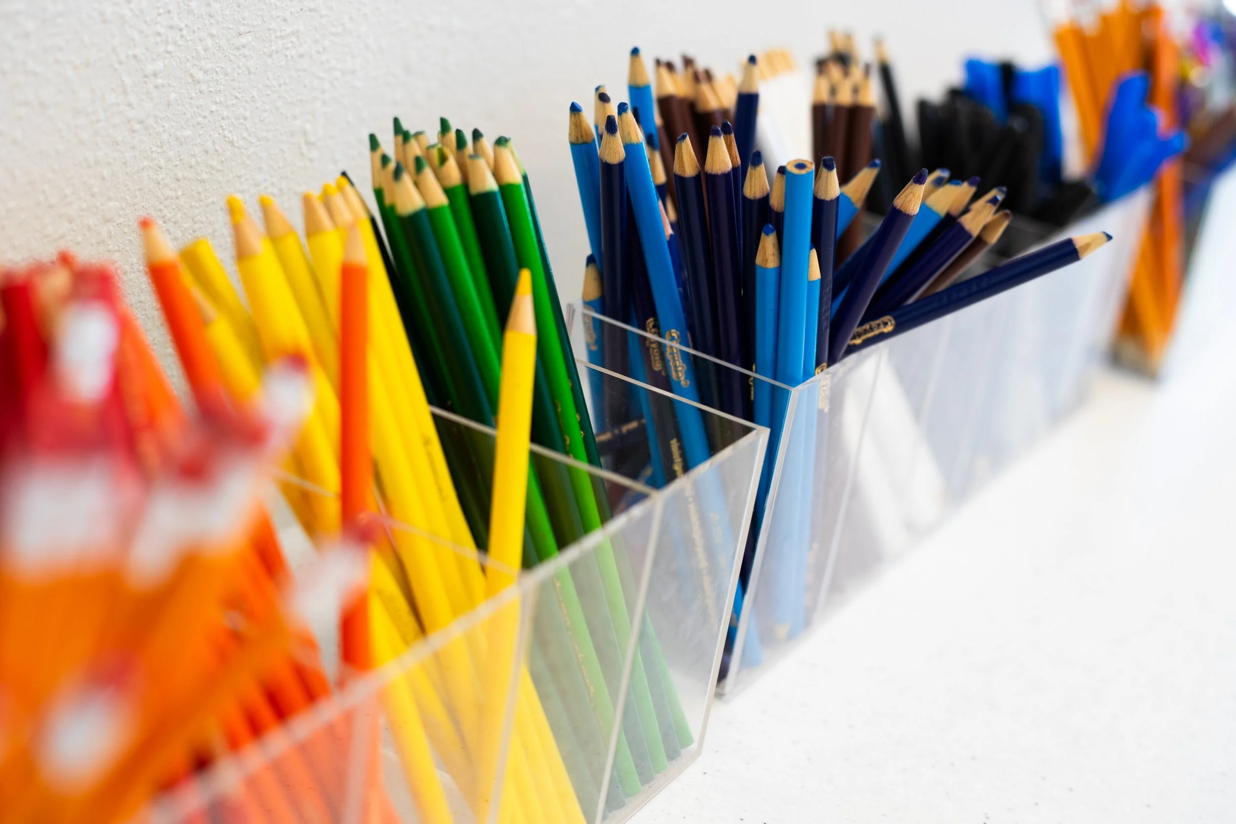 Colorful pencils sorted in transparent containers, arranged in a row, on a white surface