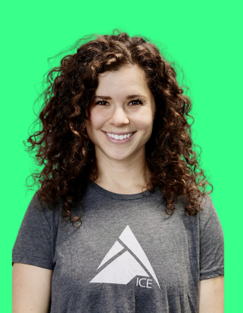 A smiling woman with curly hair wearing a gray t-shirt with an ICE logo in front of a green screen background.