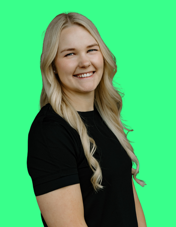 A young woman with long blonde hair smiling, wearing a black shirt, standing against a green screen background.