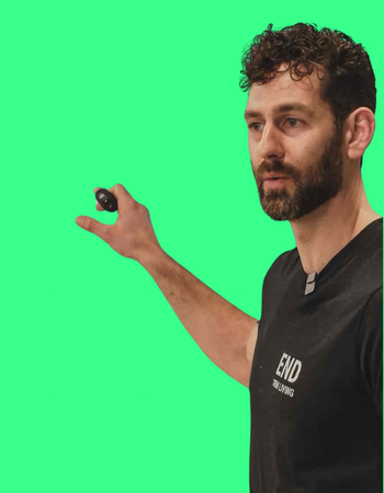 A man with curly hair and a beard holding a remote control against a green screen background.