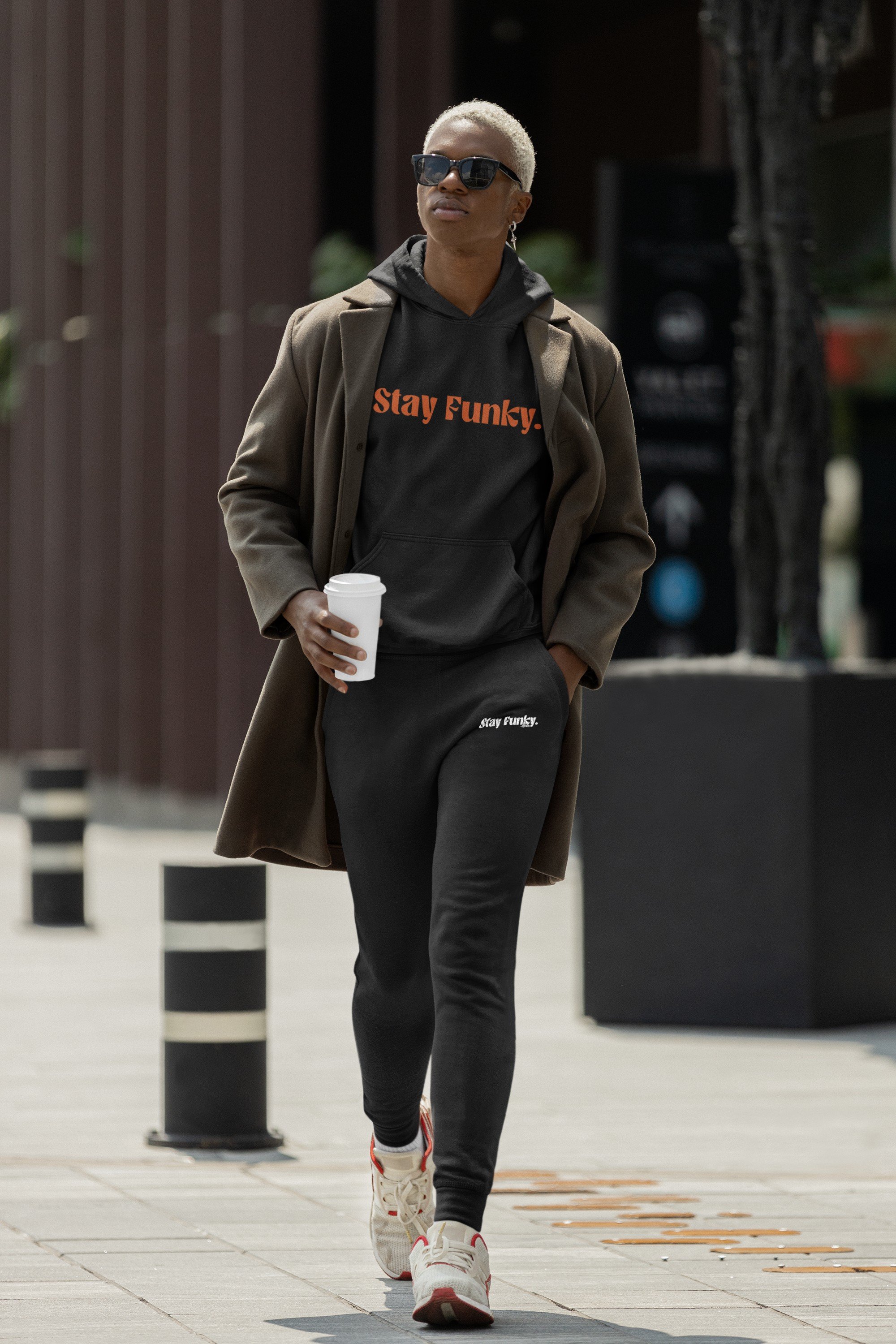 Model walking downtown in the black Secret Stash Heavyweight Hoodie with orange Stay Funky embroidery and black sweats, the Heavyweight Black set