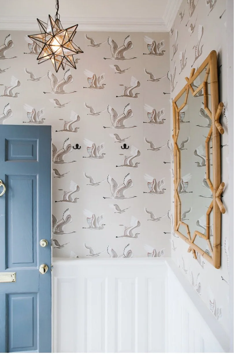 Interior corner with wallpaper featuring flying geese pattern, a blue door partially open, a star-shaped pendant light fixture, and a bamboo and wood mirror frame.