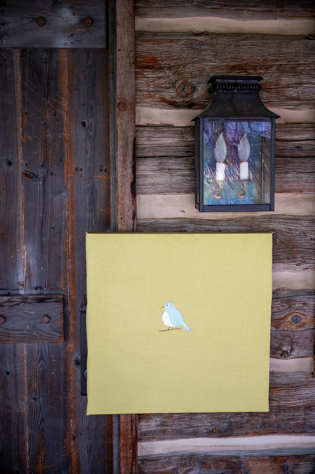 A wooden exterior wall with a black lantern and a yellow fabric with a small bird illustration.