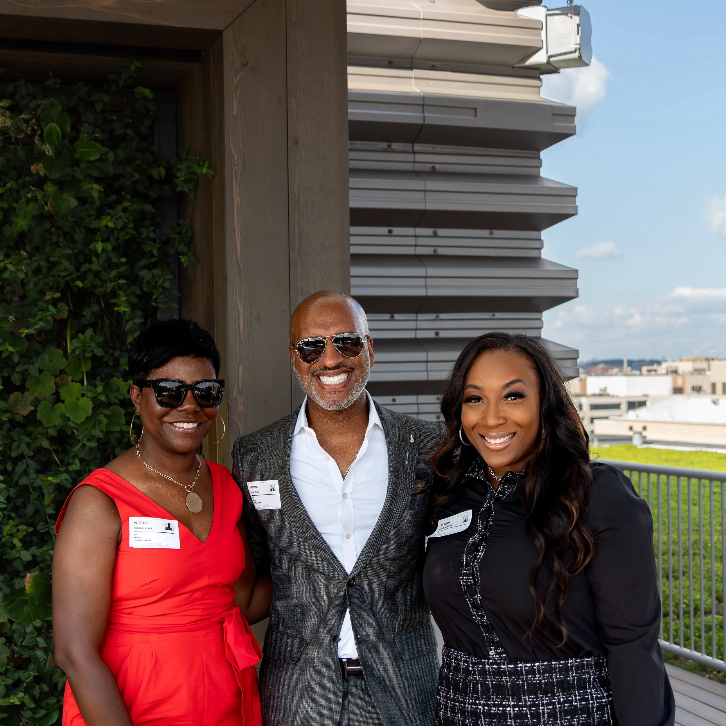 Three professionally dressed people smiling outdoors with city skyline in the background.