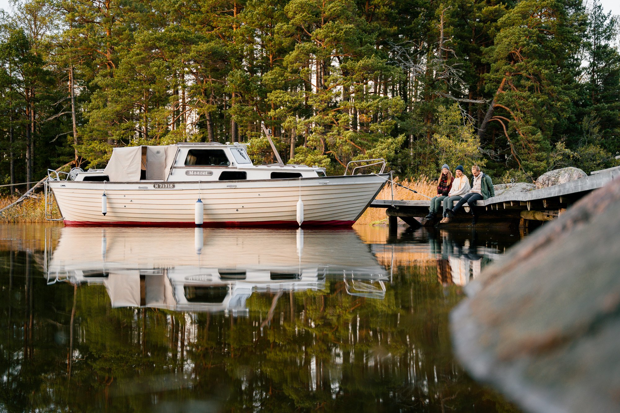 Three people sitting on a pier next to a docked boat_Finland_Finnish archipleago_Commercial photography_Kirkkonummi©Sami Laitinen.jpg