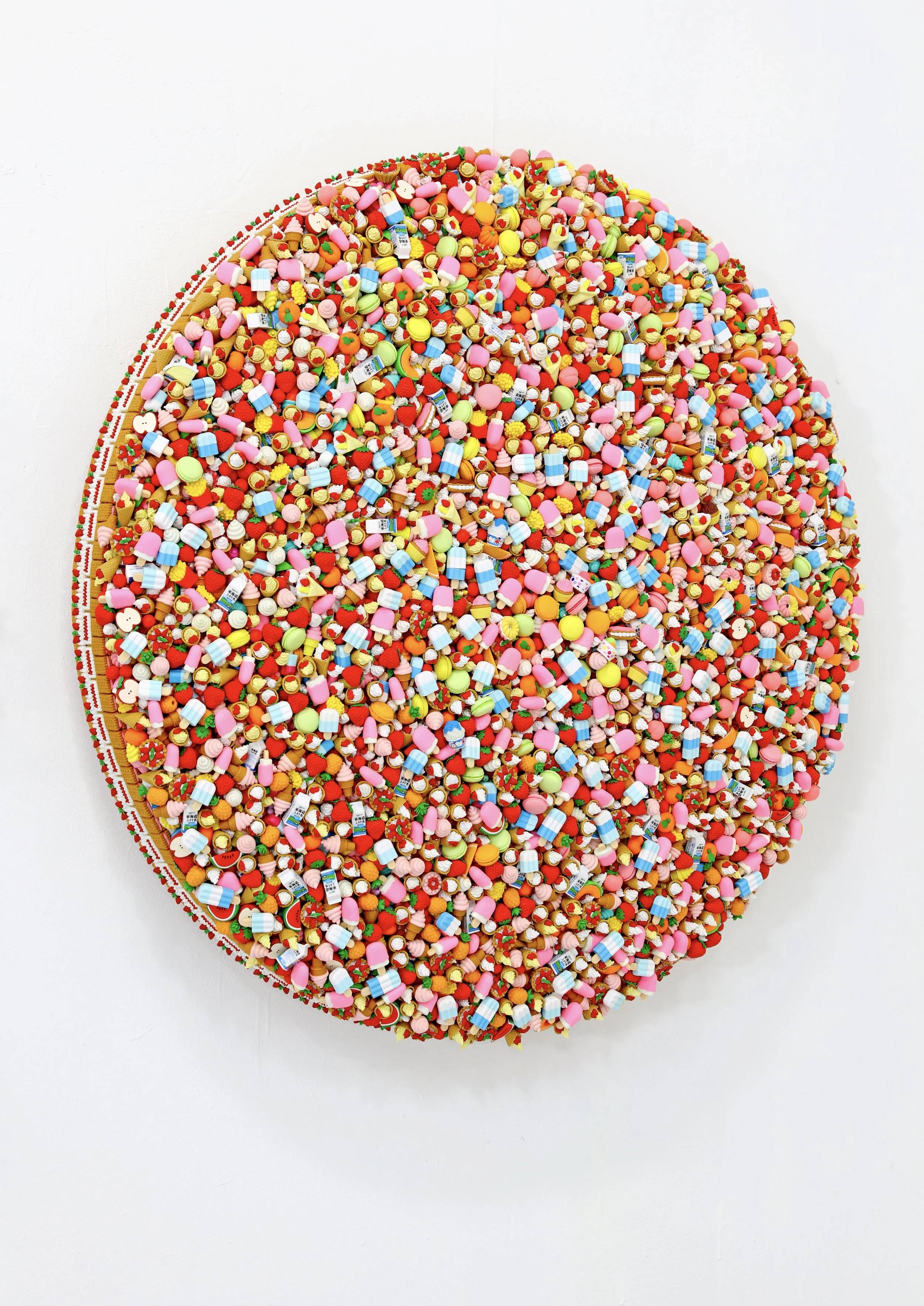 A colorful circular art piece made from tiny objects like candies, pills, and small toys assembled on a round canvas.