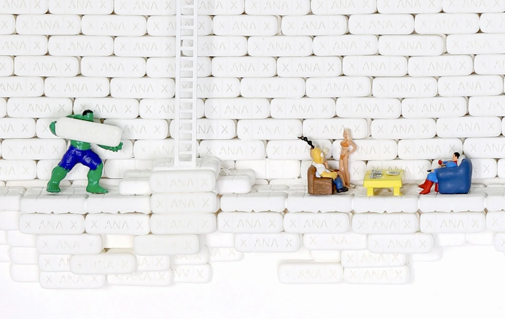 Miniature figures on soap bar surface depicting a scene with a Hulk-like figure pushing a large white object, a seated man, a standing nude woman, and a woman sitting on a chair watching TV