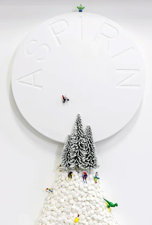 Decorative clock face with large embossed letters spelling 'ASCIPRN' and a small green alien figure at the top. Below the clock, there are snow-covered toy trees and miniature figurines of skiers and a green toy dinosaur, creating a winter scene.