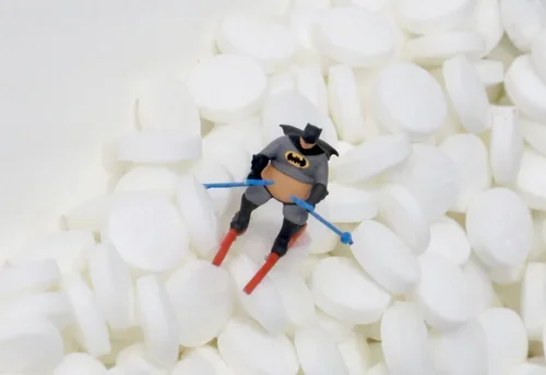 Small Batman toy figure skiing on a bed of white marshmallows.
