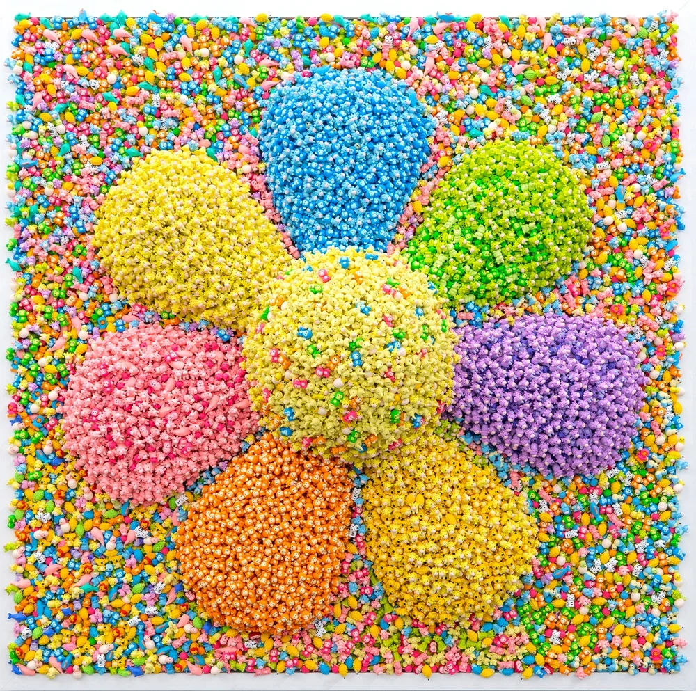 Colorful Easter egg sculptures made of small candies arranged on a square background covered with tiny candies in various bright colors.