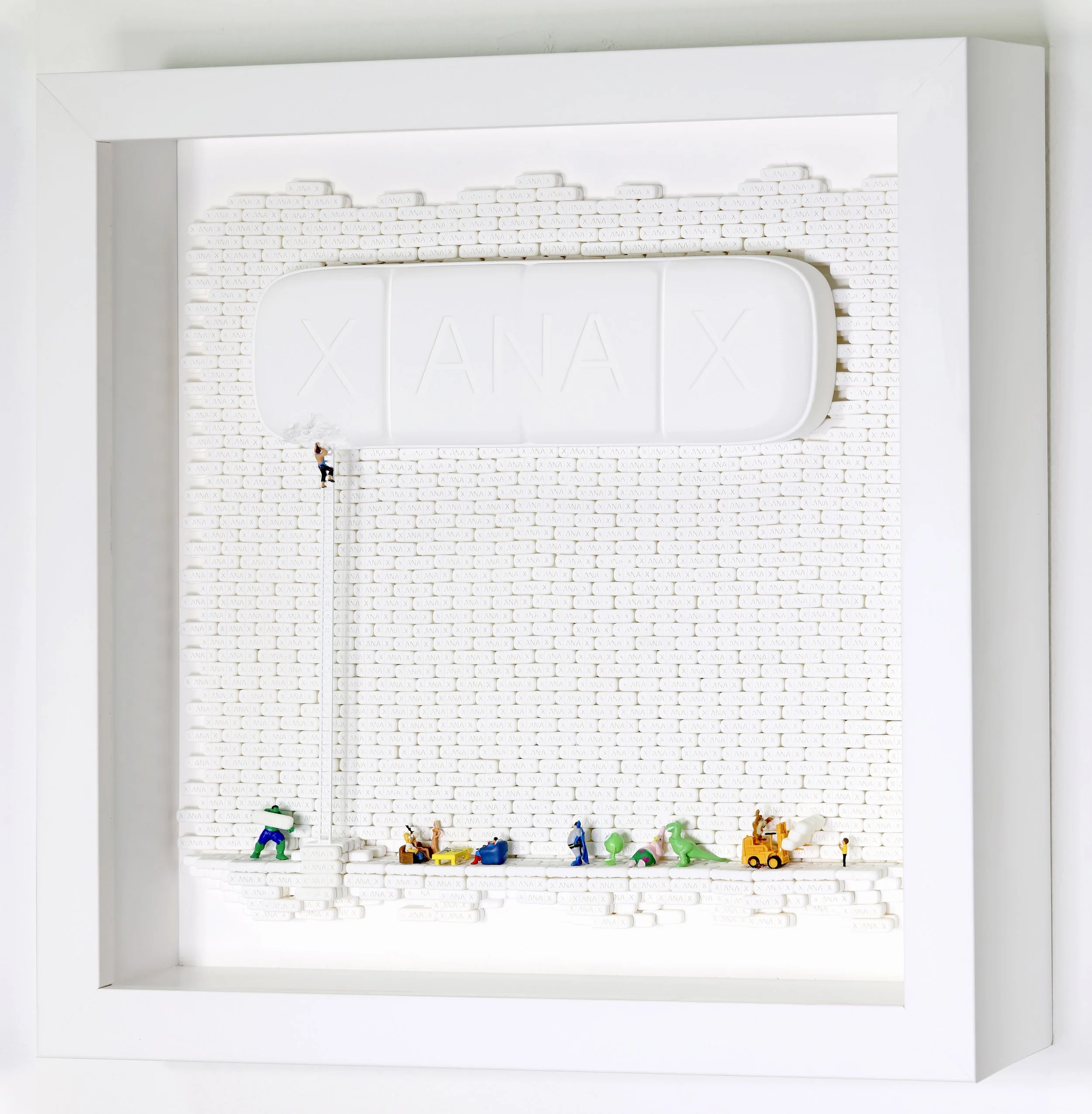 Miniature figurines of construction workers and tools arranged against a white brick wall, with a large sign reading 'XANAX' at the top.